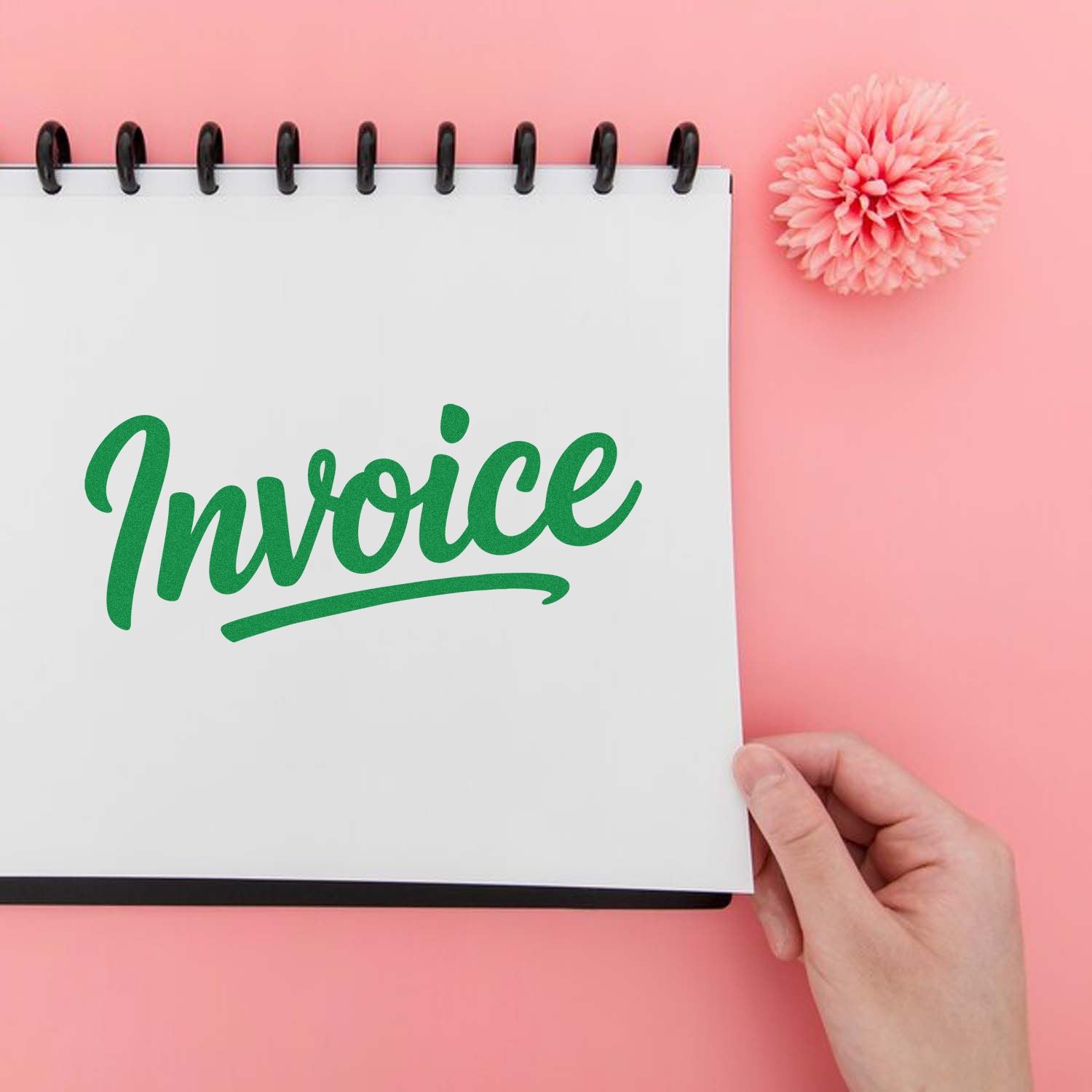 Green invoice stamp on white spiral notebook with black binding, held over a pink background beside a pink flower seal.