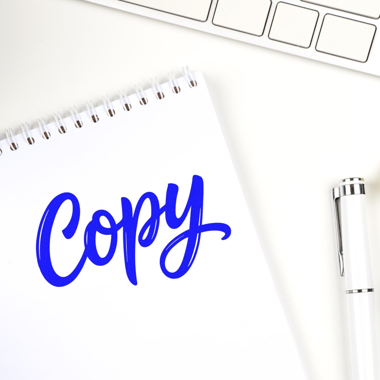 Blue Copy stamp on white spiral notebook beside a white pen and laptop keyboard, showcasing custom stamp and seal products.