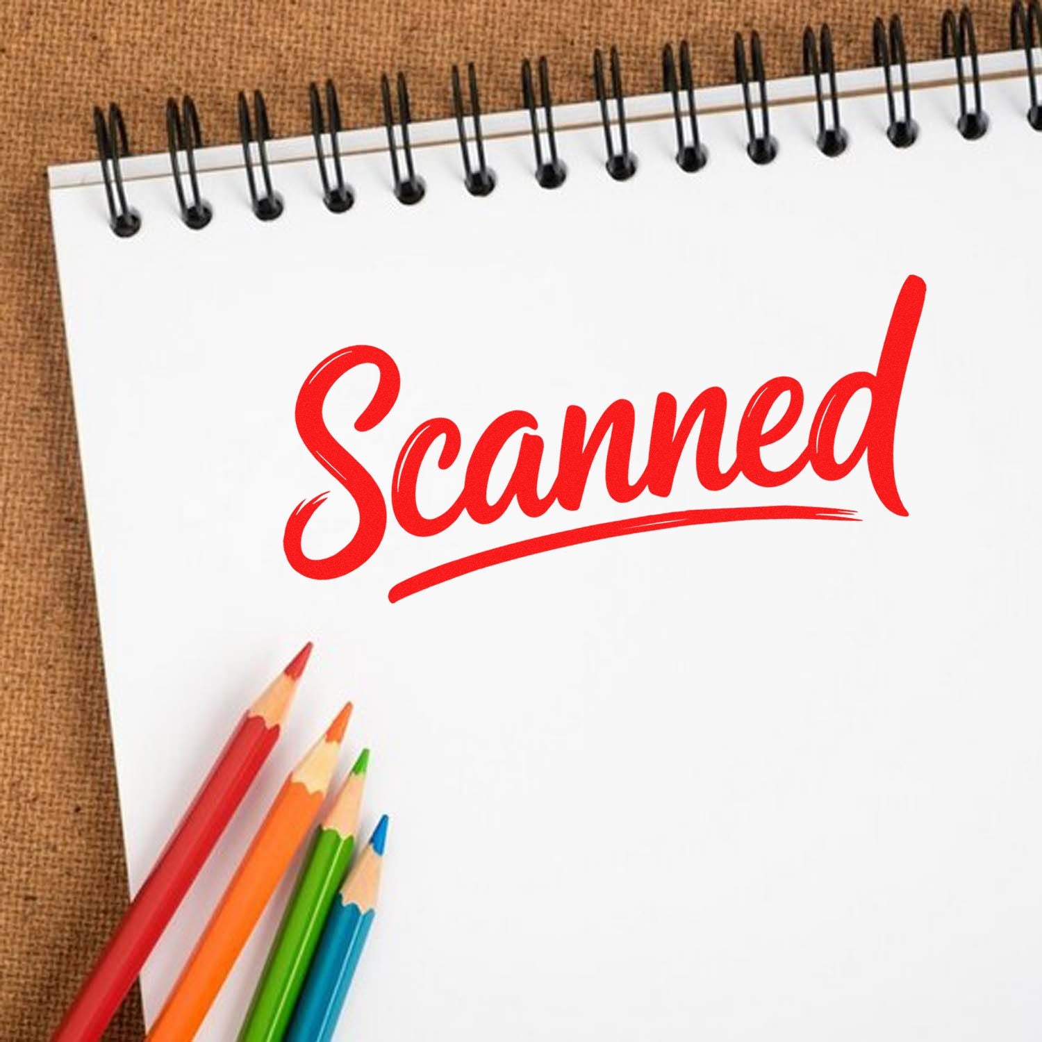 Red scanned rubber stamp seal on white spiral notebook with colorful pencils on a brown textured background.