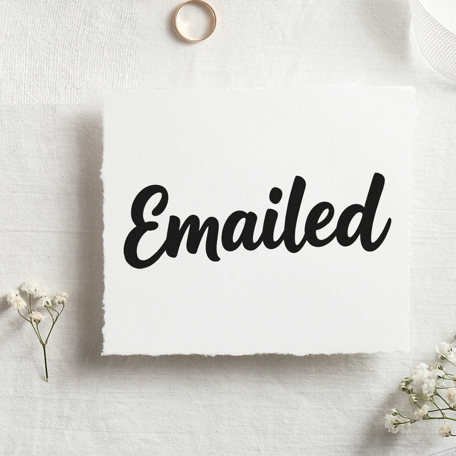 Black Emailed rubber stamp on white textured paper, styled with delicate white flowers on beige fabric.