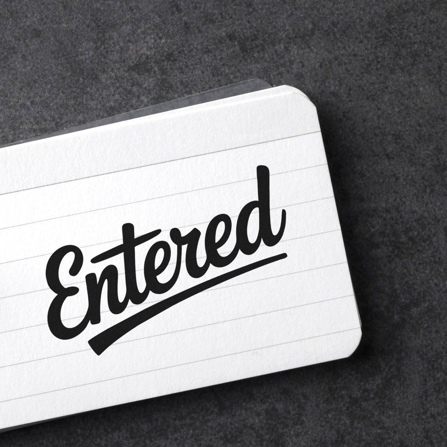 Black Entered stamp seal on a white lined card against a dark textured background.