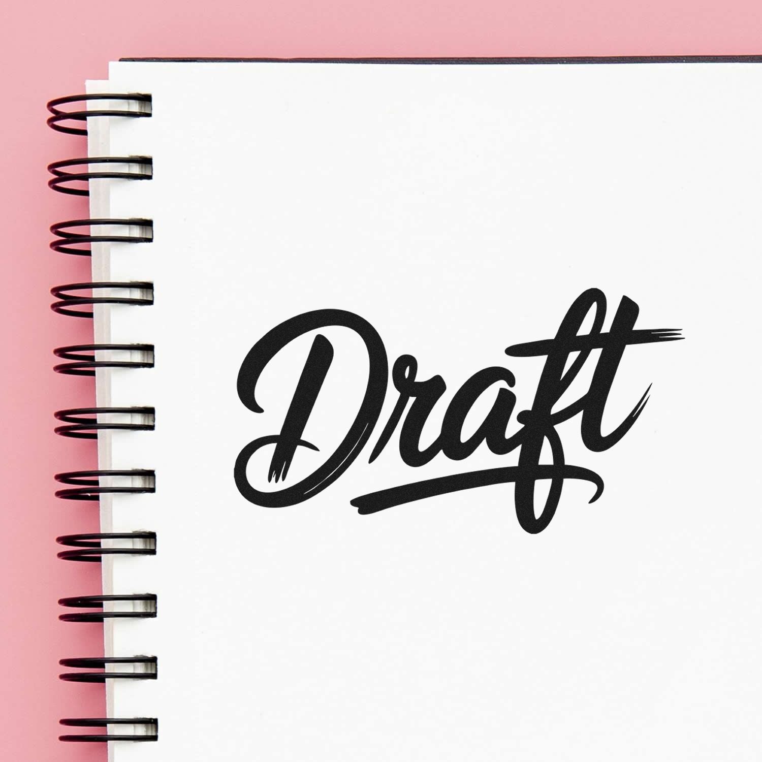 White spiral notebook with black Draft stamp and seal mark on the cover, against a pink background.