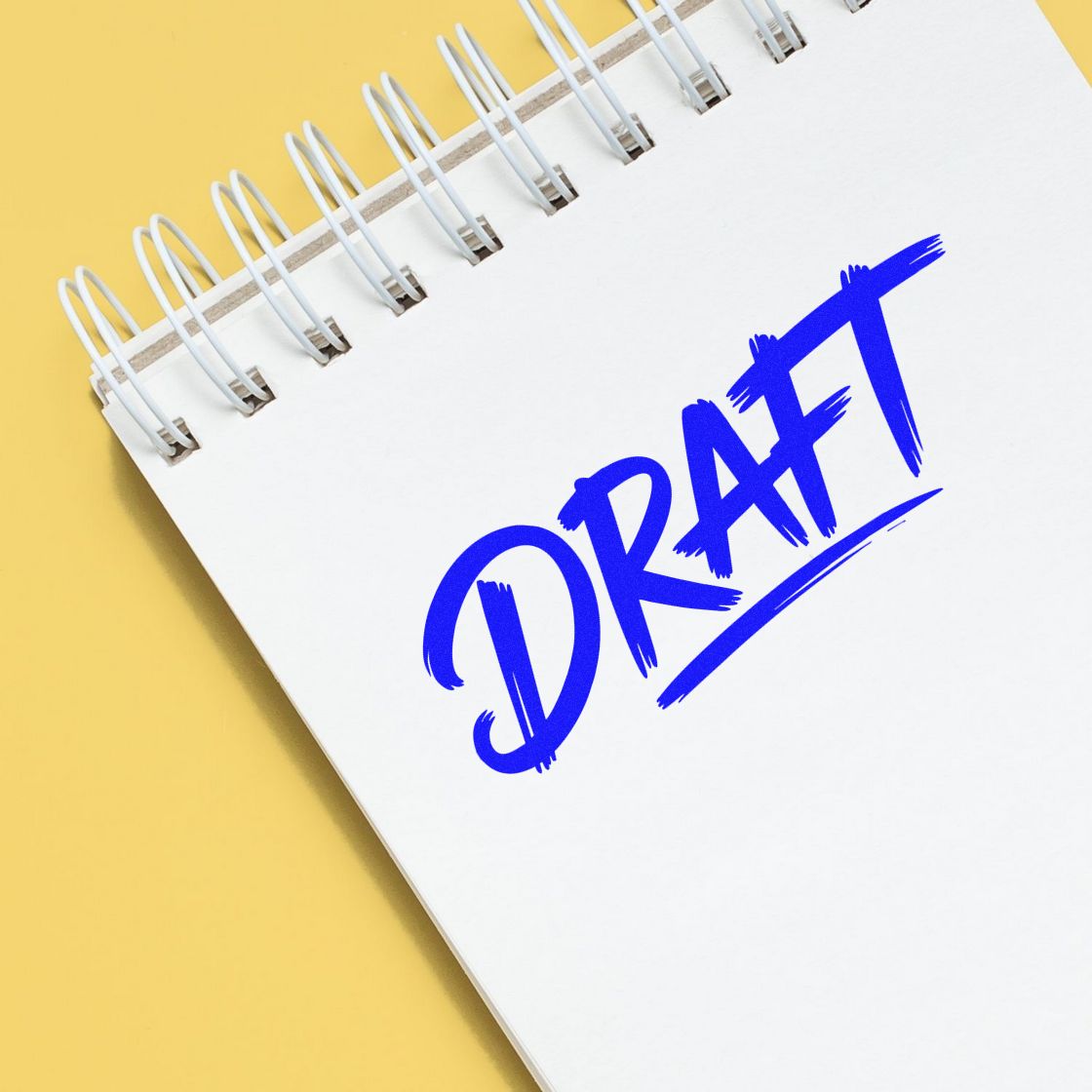 Blue DRAFT stamp seal on a white spiral notebook, set against a bright yellow background.