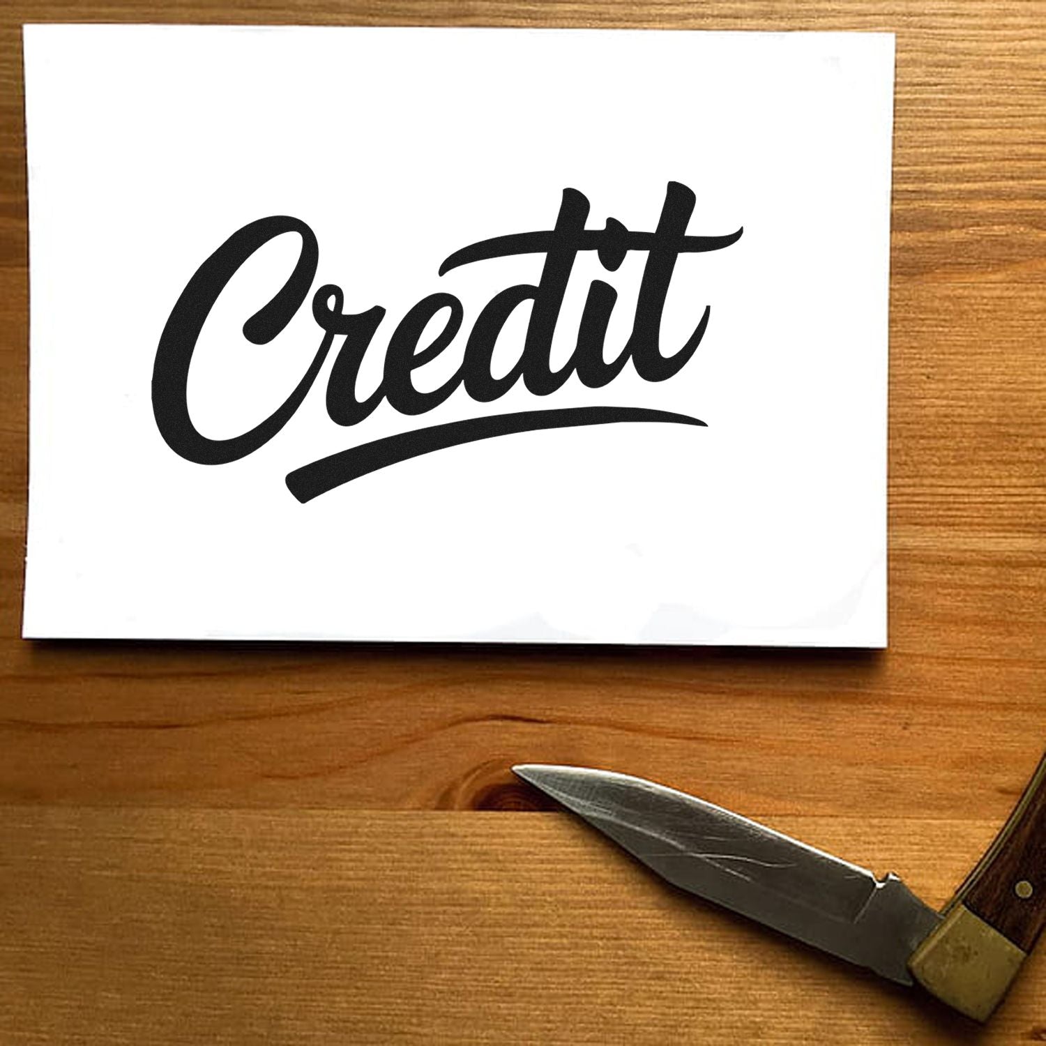 Black Credit script stamp and seal on white card beside a silver pocketknife on a wood table.