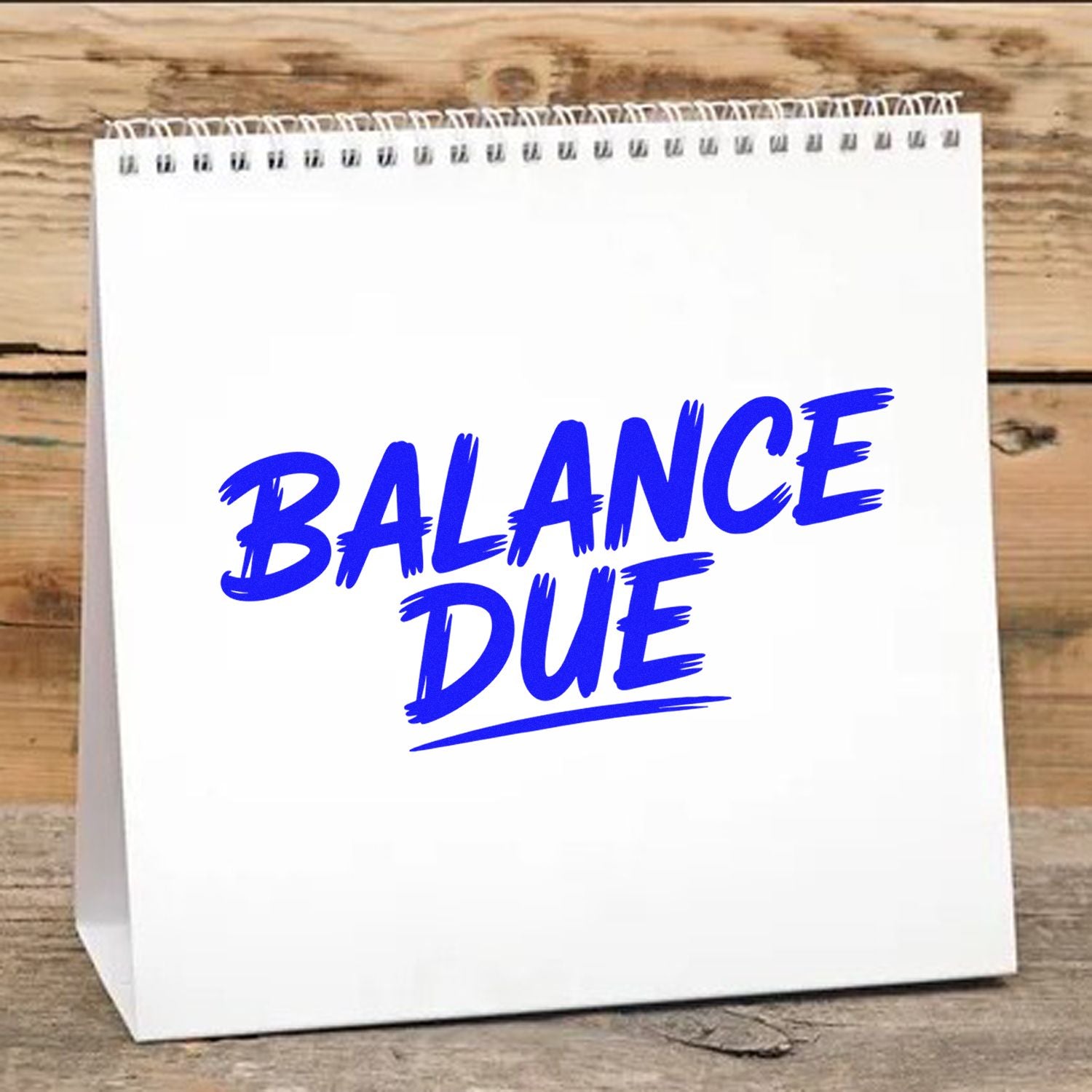 White spiral-bound stamp and seal product with bold blue BALANCE DUE lettering on a rustic wood background.