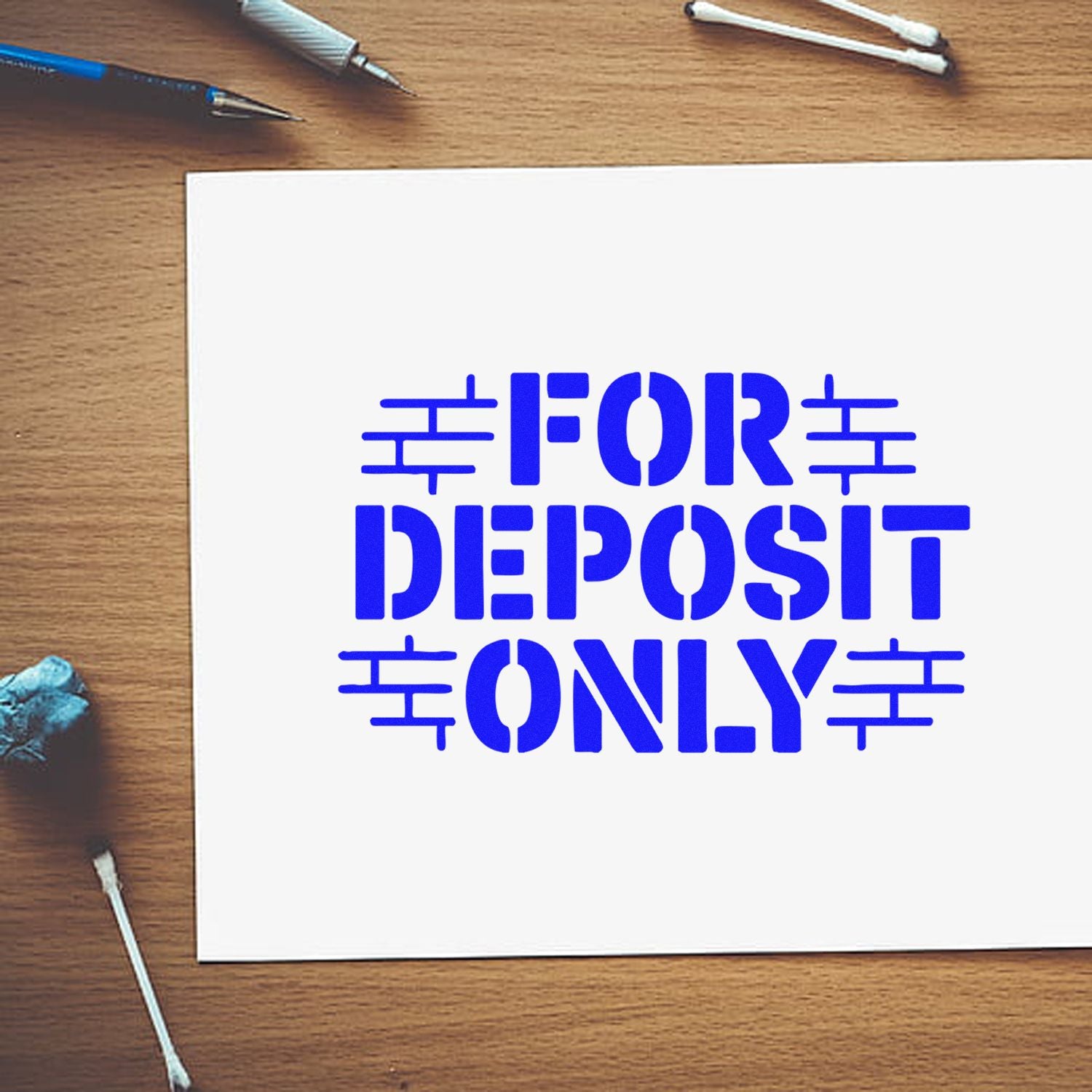 Blue FOR DEPOSIT ONLY stamp seal on white paper, with pens and cotton swabs on a wood desk.