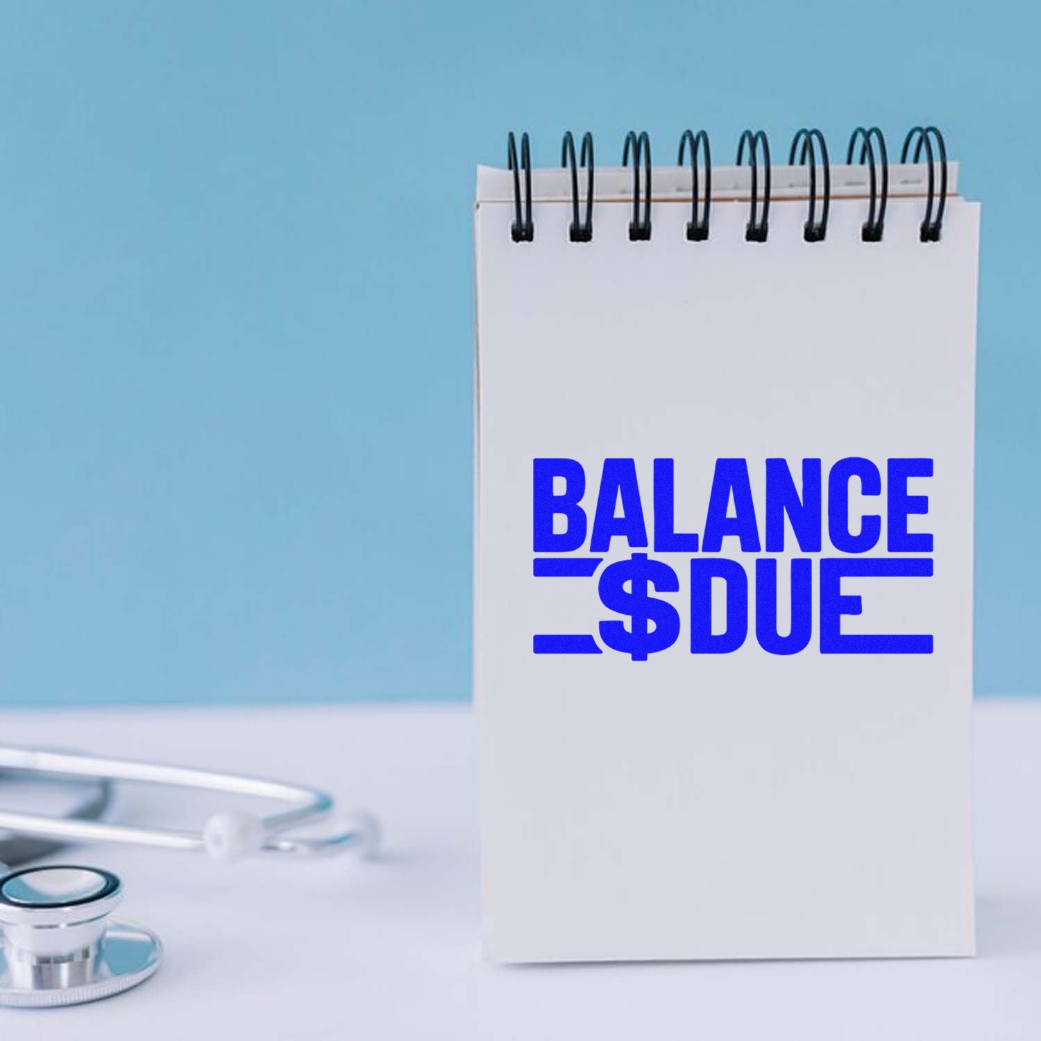 Blue balance due stamp seal on a spiral notebook beside a stethoscope, against a light blue background