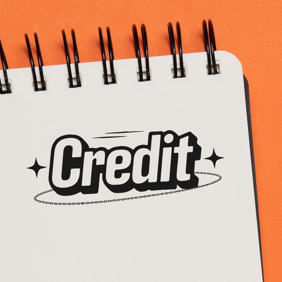 Black credit stamp and seal design with chain underline and stars on a white spiral notebook, against an orange background.