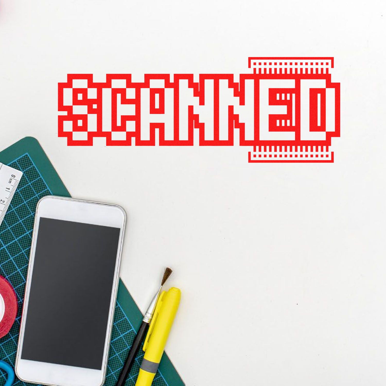 Red pixel-style SCANNED stamp with seal border on white, beside cutting mat, smartphone, brush and yellow marker.