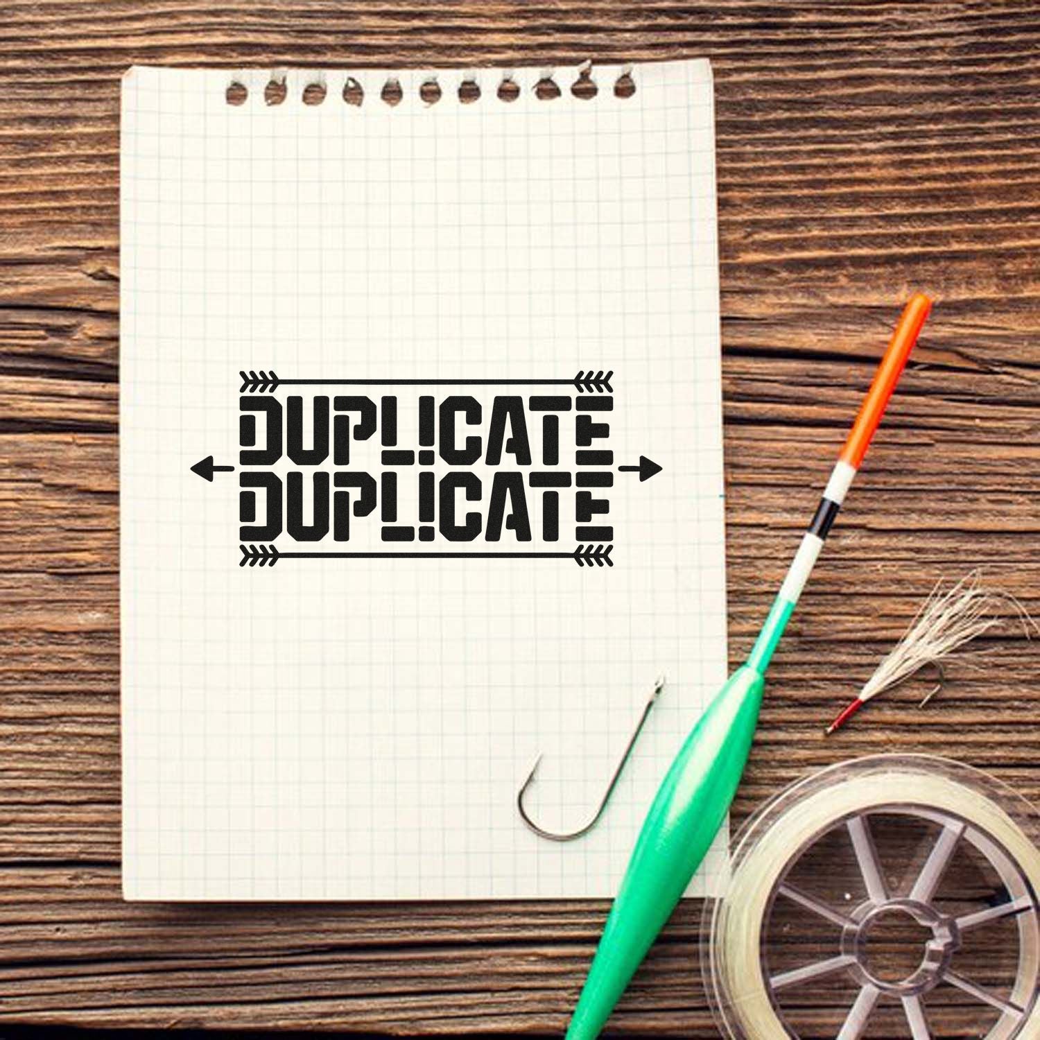 Black DUPLICATE stamp and seal design on graph paper notebook, with fishing hook, lure, line spool, and orange-green tackle on wood.