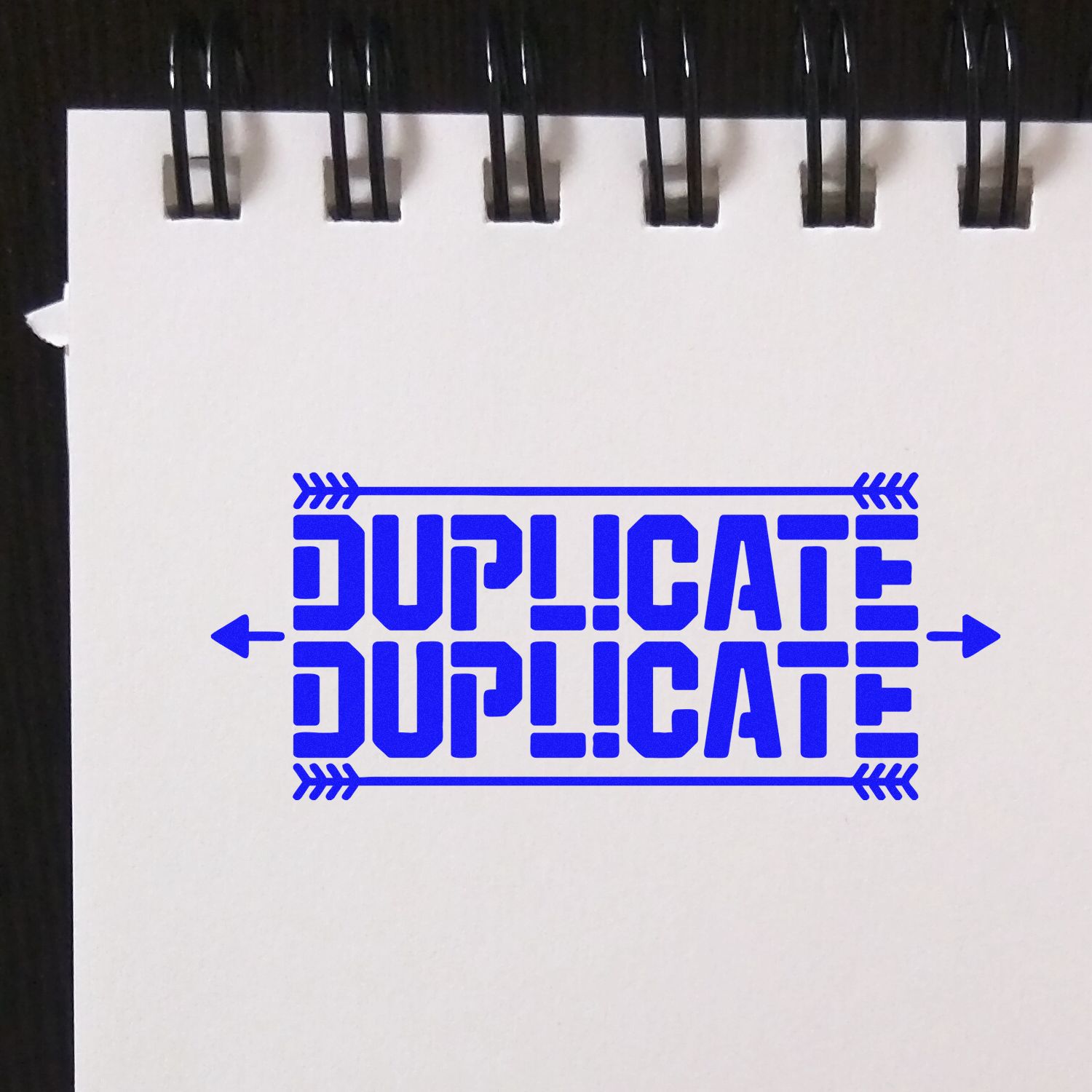 Blue DUPLICATE stamp with arrow borders on a white spiral-bound page, stamp and seal product sample.