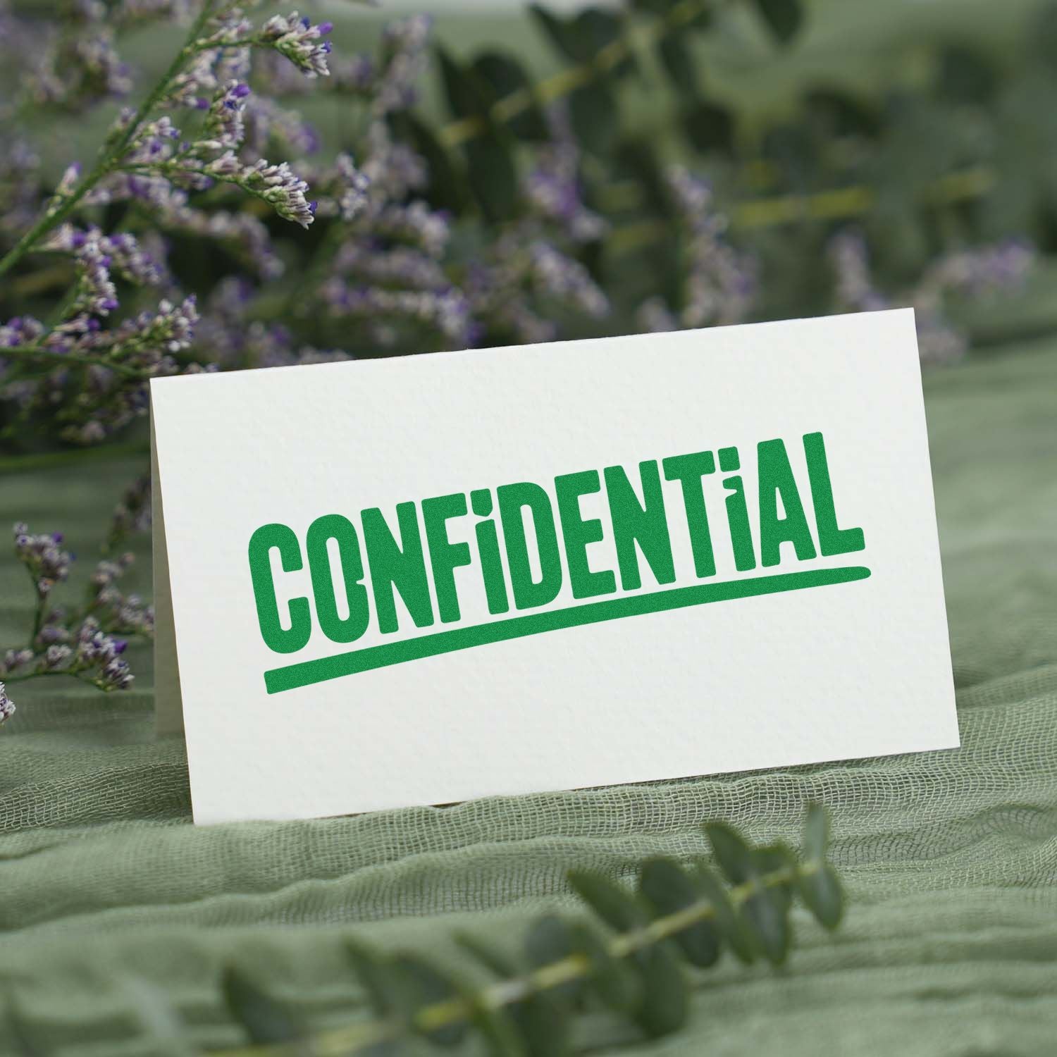 Green CONFIDENTIAL stamp seal on white card, with blurred purple flowers and green mesh background.
