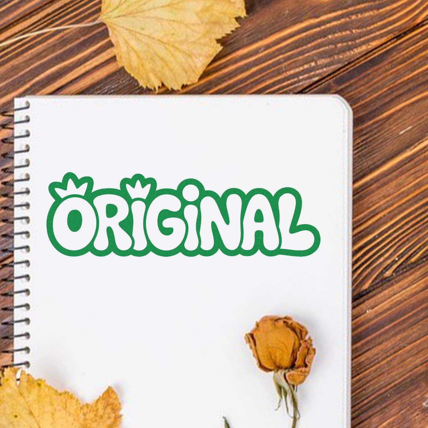 Green ORIGINAL stamp seal on a white spiral notebook, with dried leaves on a wood table.