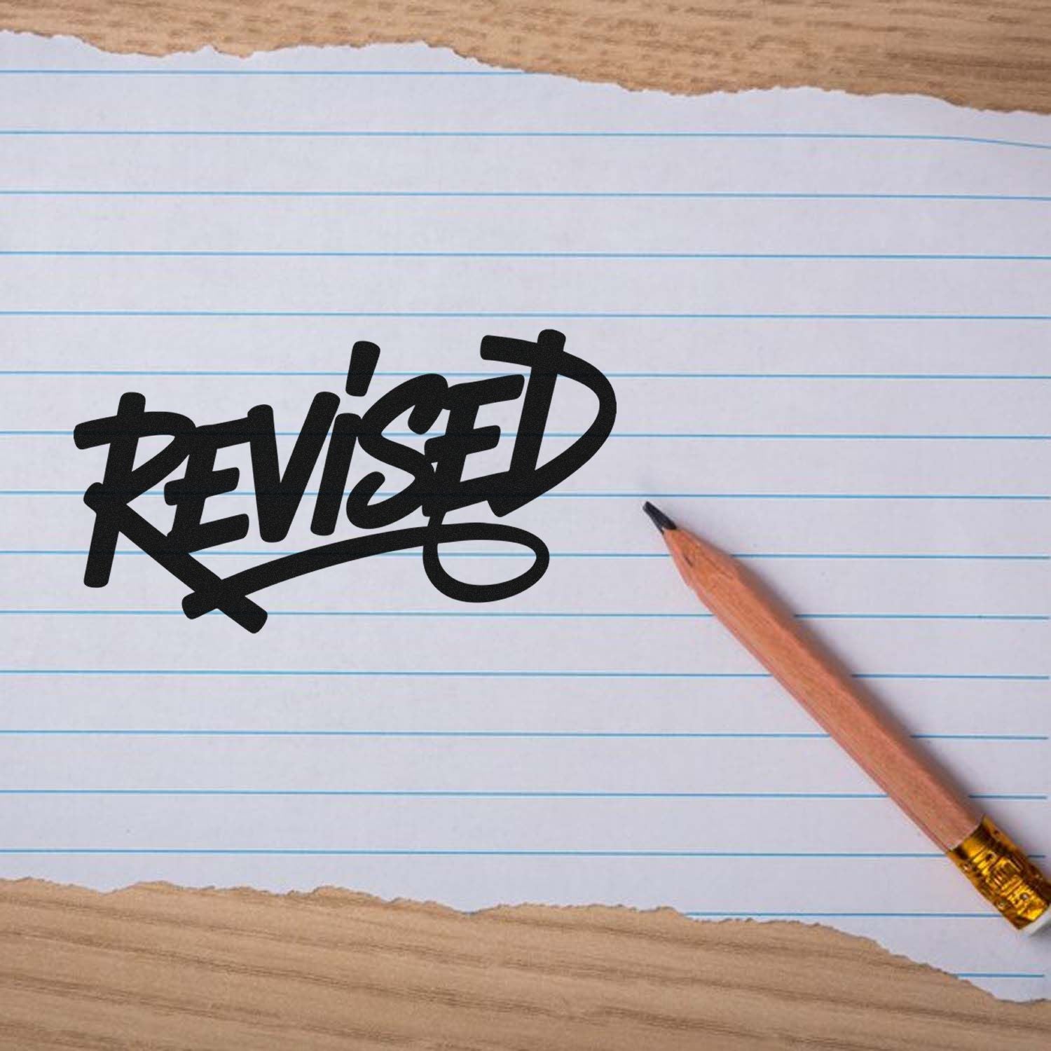 Black REVISED stamp seal on lined white paper beside a wooden pencil.