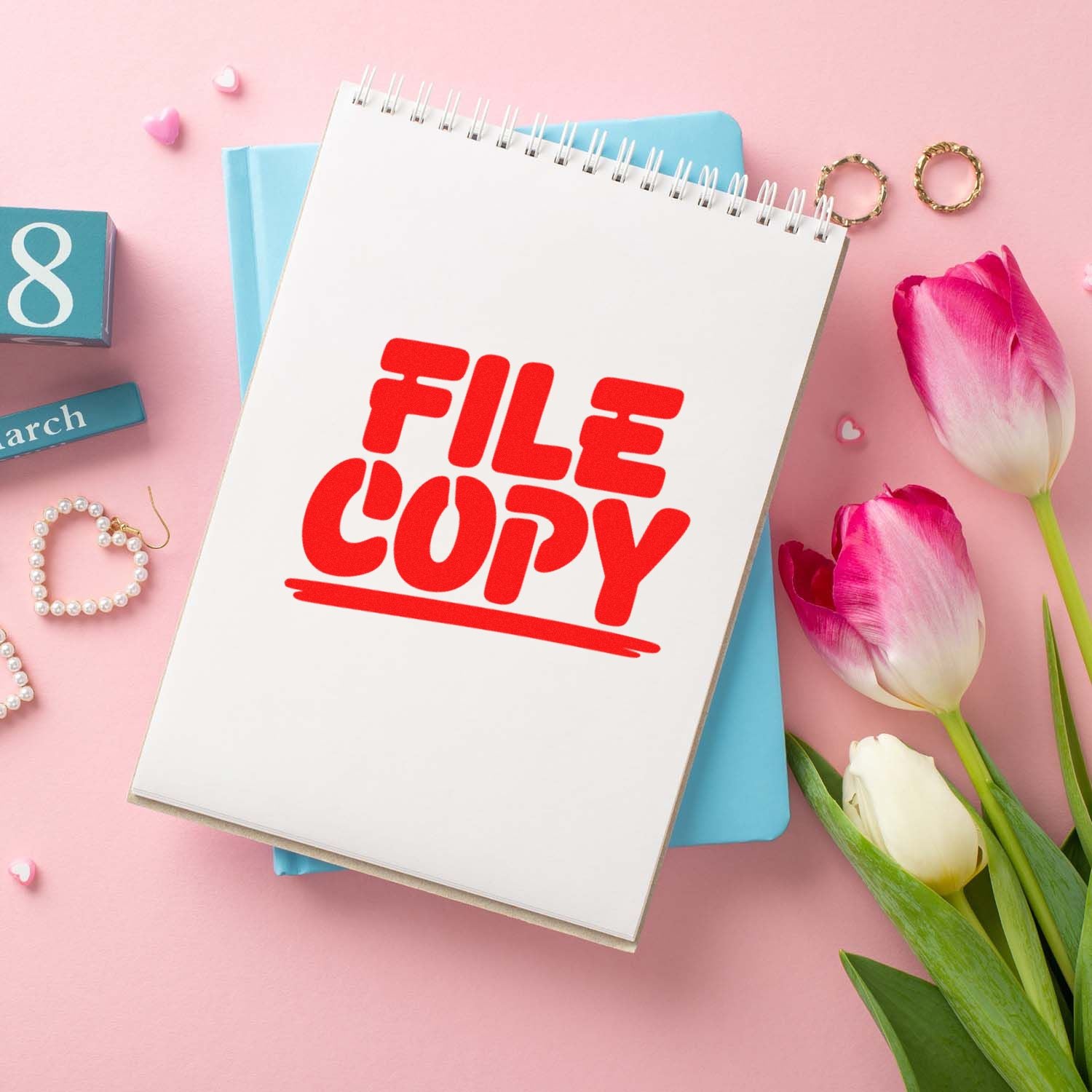 Red FILE COPY stamp seal on white spiral notepad, with pink background, blue notebook, tulips, and gold rings.