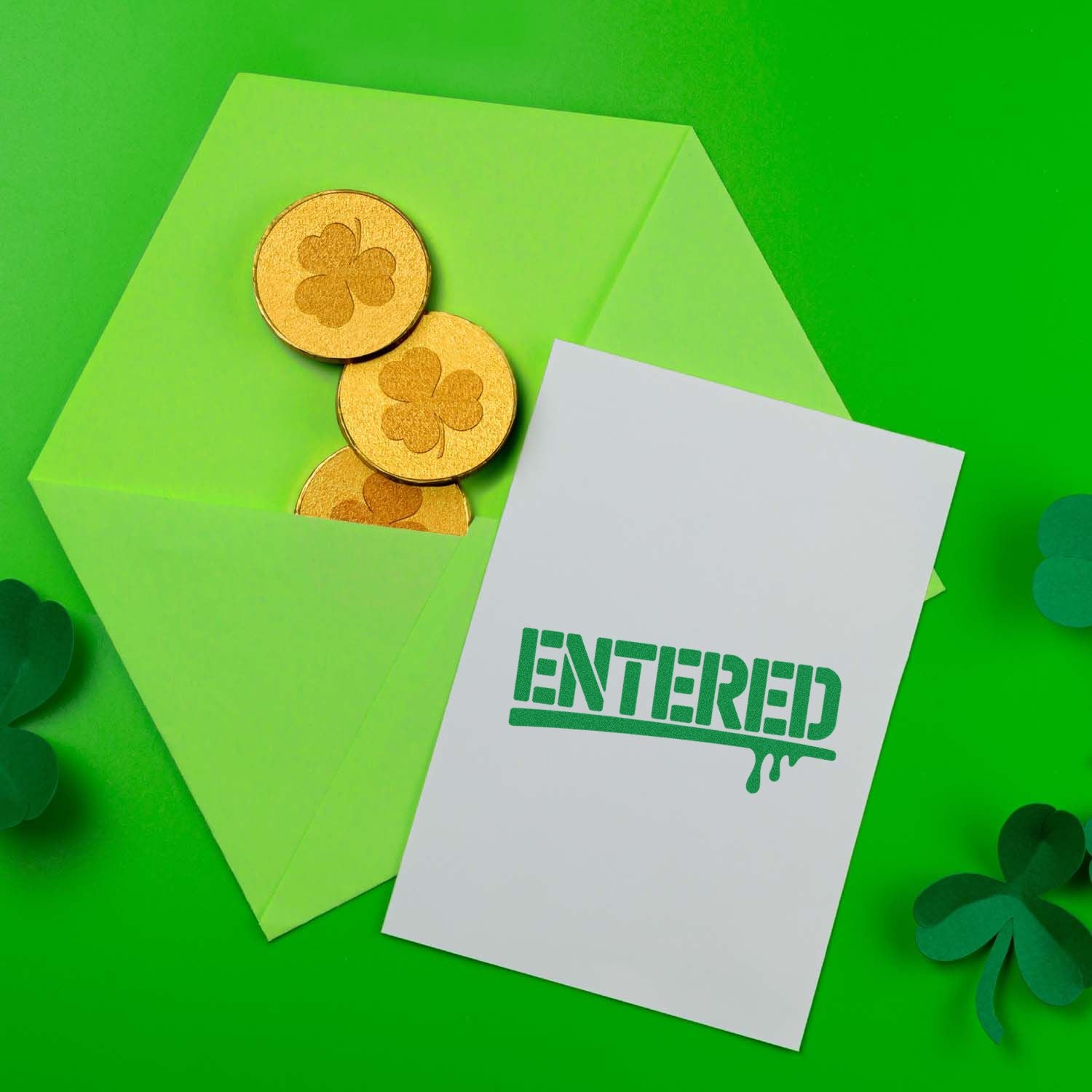 Green envelope with gold shamrock seal stamps and a white ENTERED card on a bright green background.