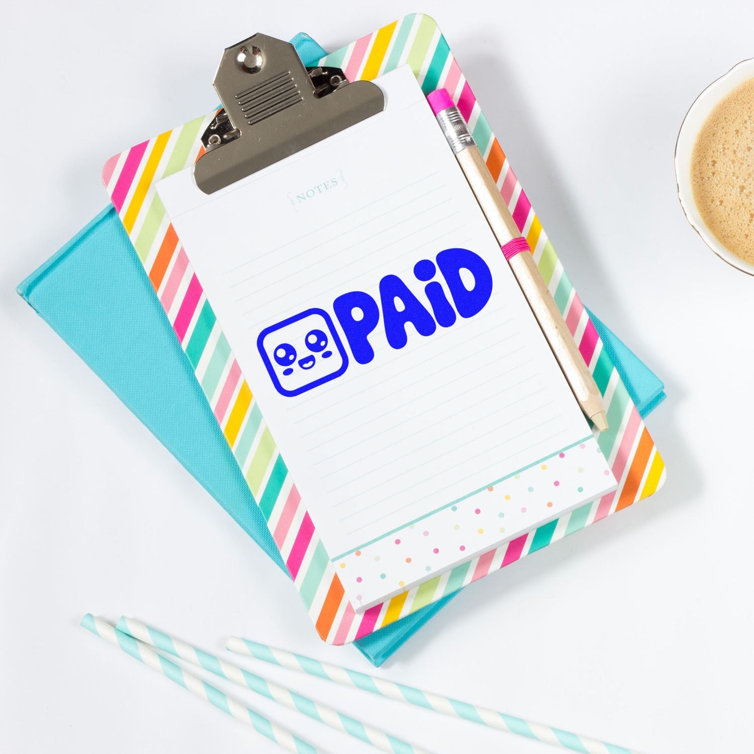 Blue PAID self-inking stamp on striped clipboard notepad with pencil, turquoise folder, and coffee cup.