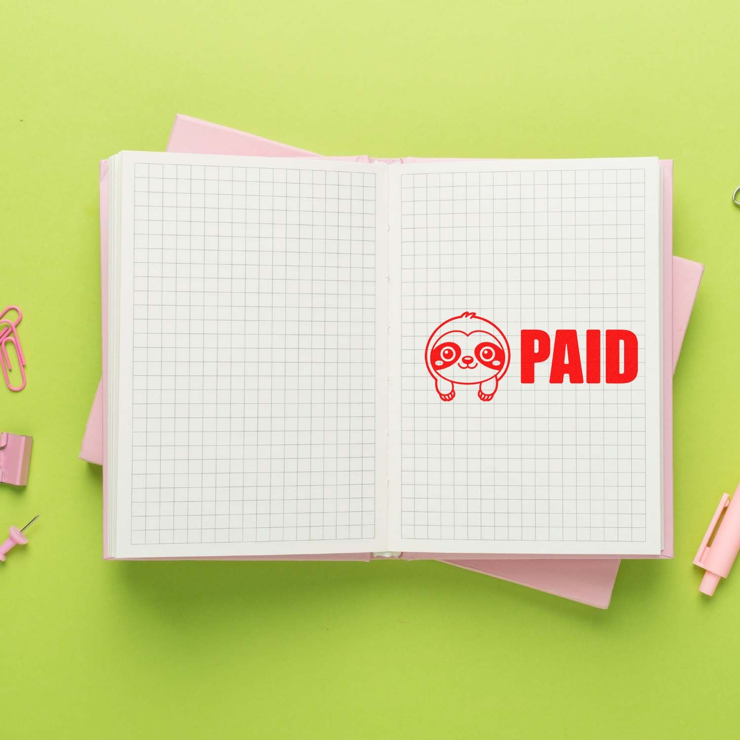 Red PAID rubber stamp with cute sloth seal on open grid notebook, on lime green background