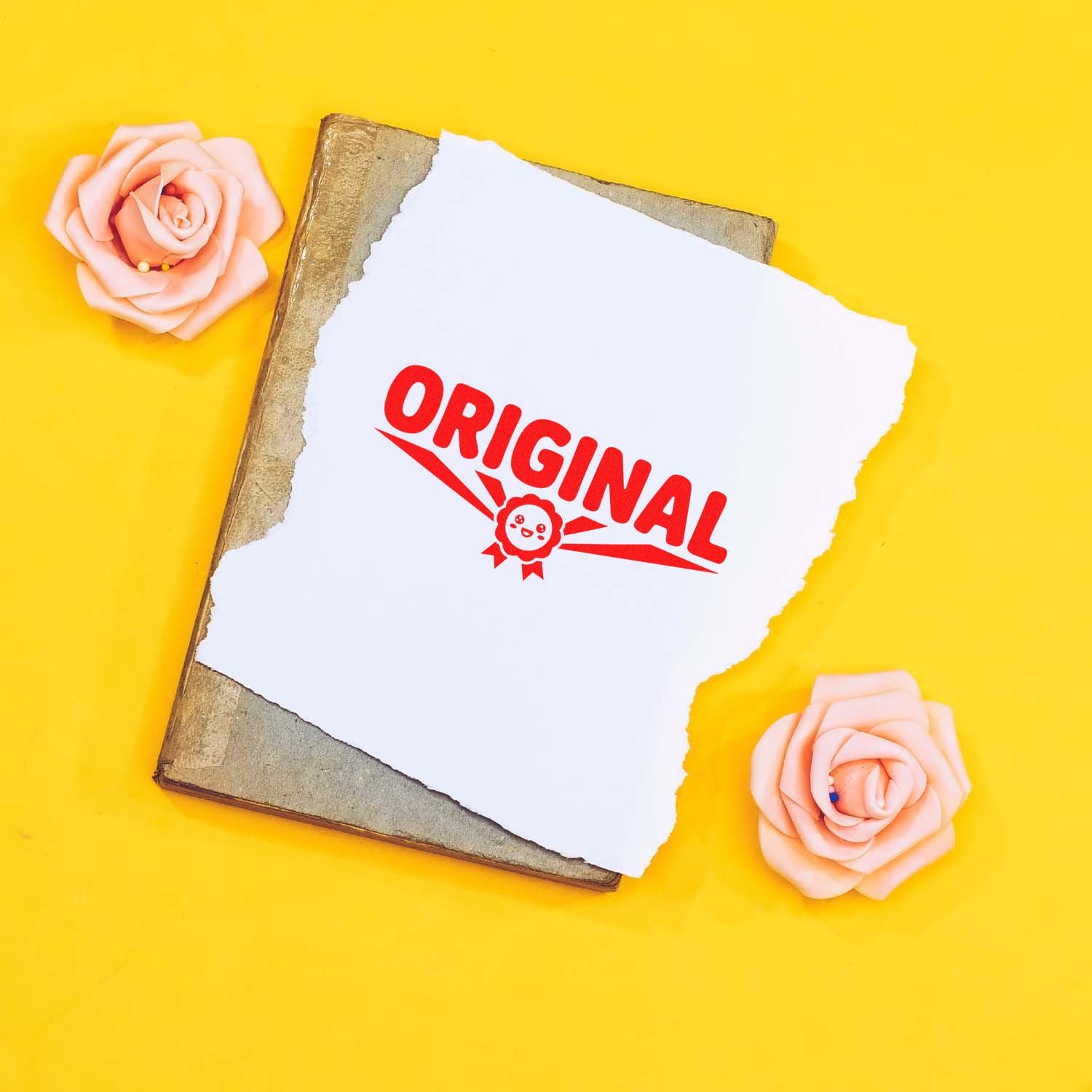 Red ORIGINAL stamp on torn white paper over vintage book, with pink rose seal accents on a bright yellow background.