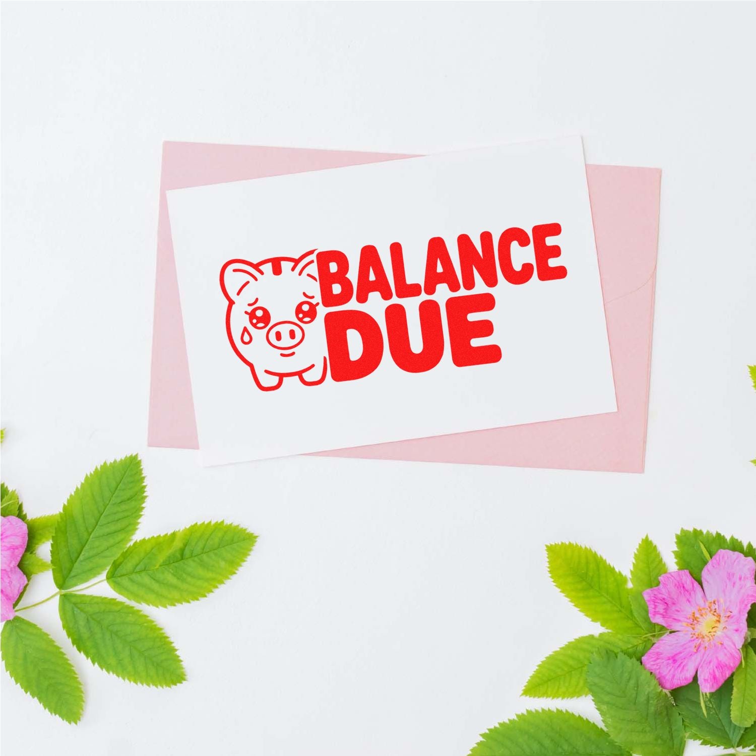 Red BALANCE DUE pig stamp seal on white card, layered over pink paper, with green leaves and pink flowers.