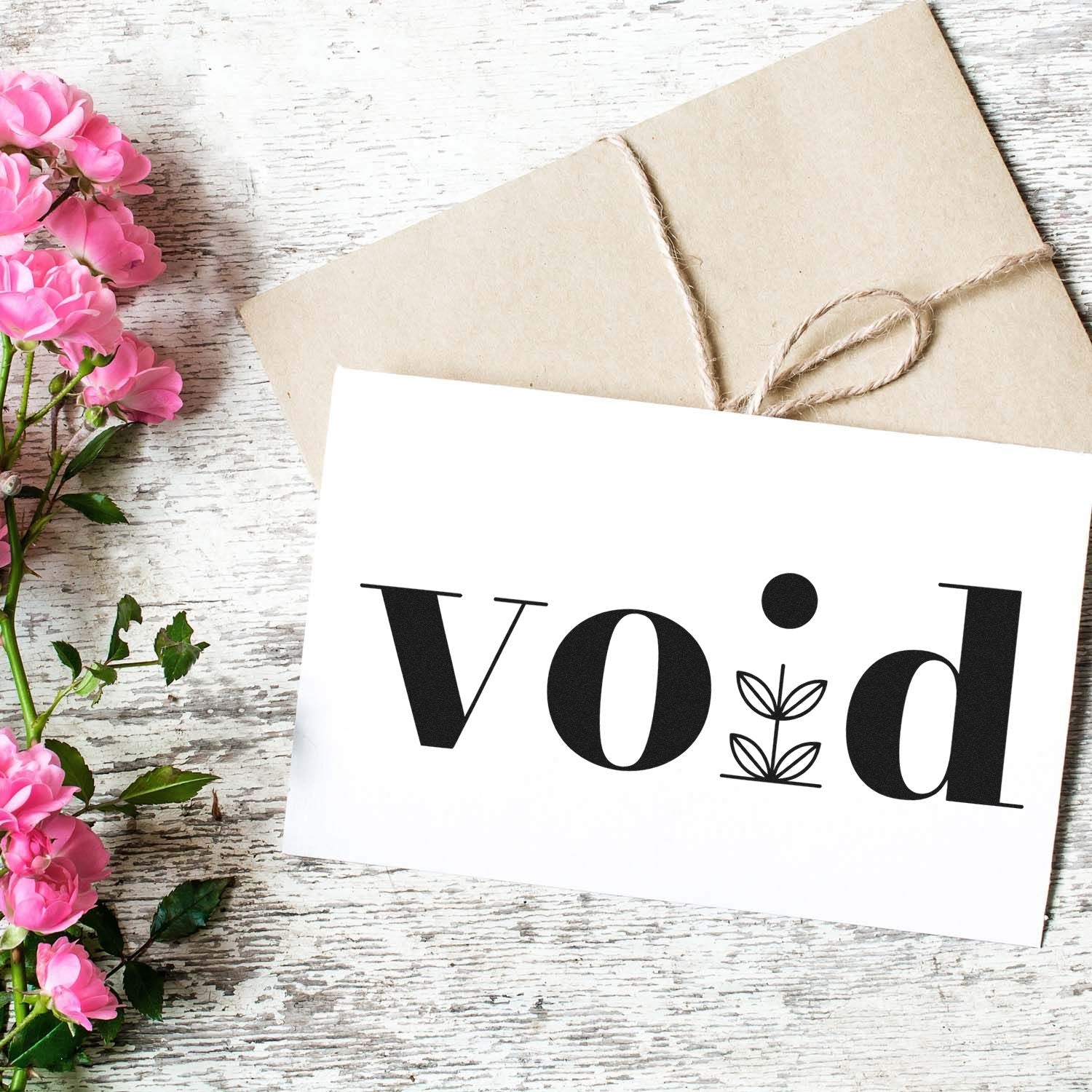 Void stamp and seal design on white card, with black leaf icon, kraft envelope twine, and pink flowers on rustic wood.