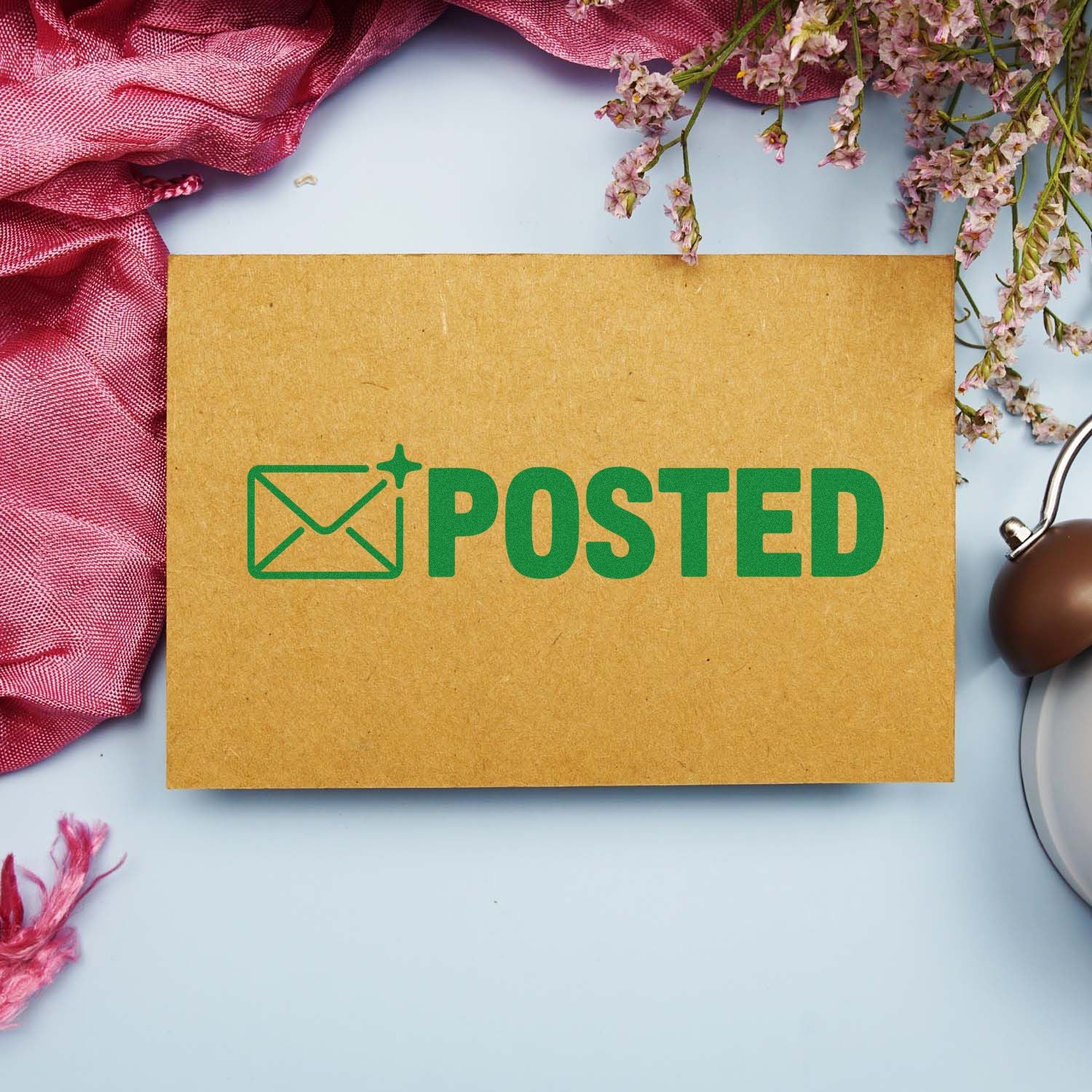 Brown kraft card featuring a green POSTED mail stamp seal, with pink fabric and flowers on a light blue background.