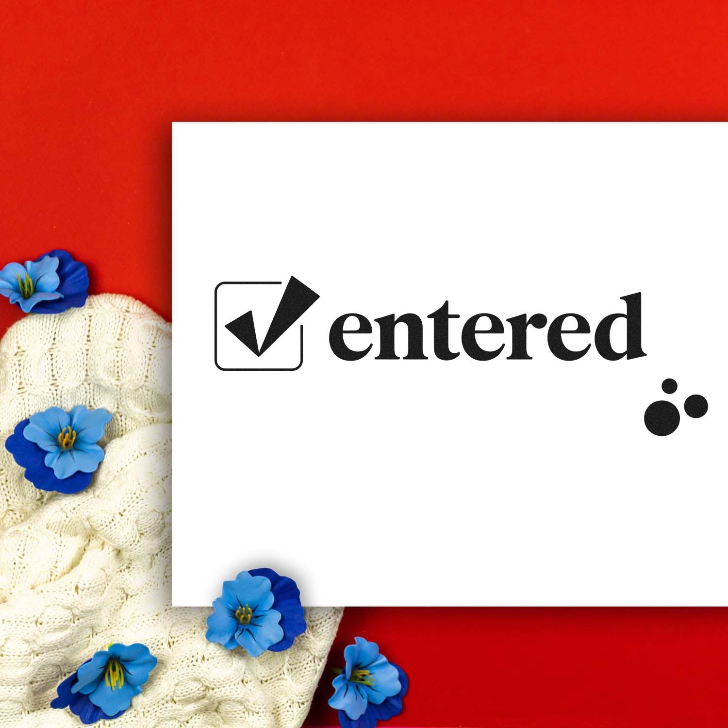 White card with black Centered stamp seal and checkmark on red background, framed by cream knit and blue flowers.