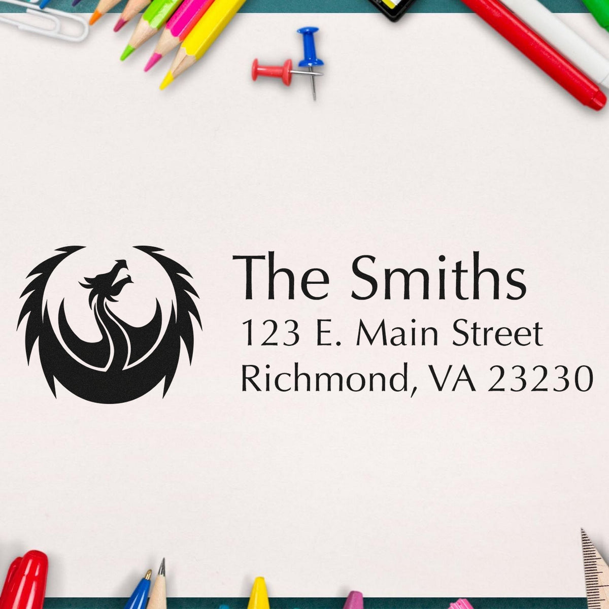 Custom black seal stamp with phoenix logo and The Smiths address, framed by colorful pencils and push pins on white paper.