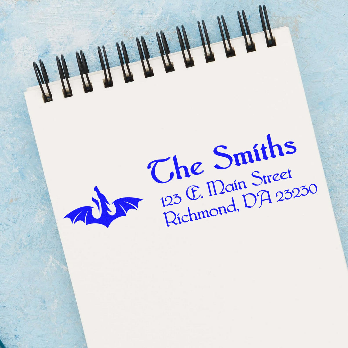 Blue custom address stamp and seal on a white spiral notepad, featuring The Smiths and a bat logo on a light blue background