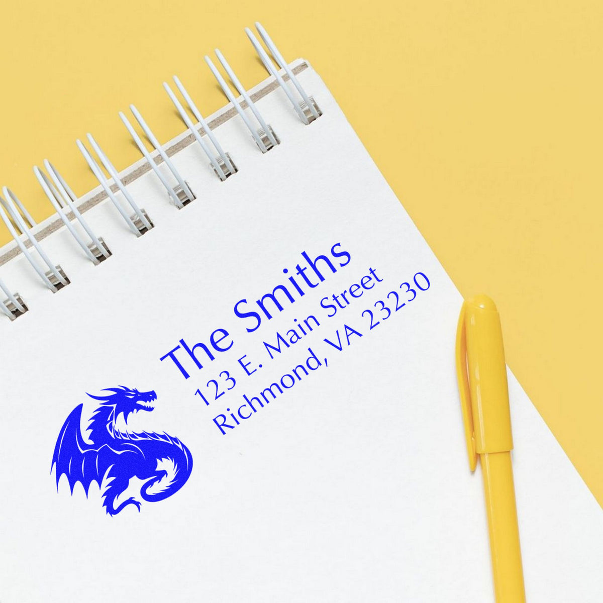 Blue business stamp and seal imprint on white notepad, with dragon logo, spiral binding, and yellow pen on yellow background