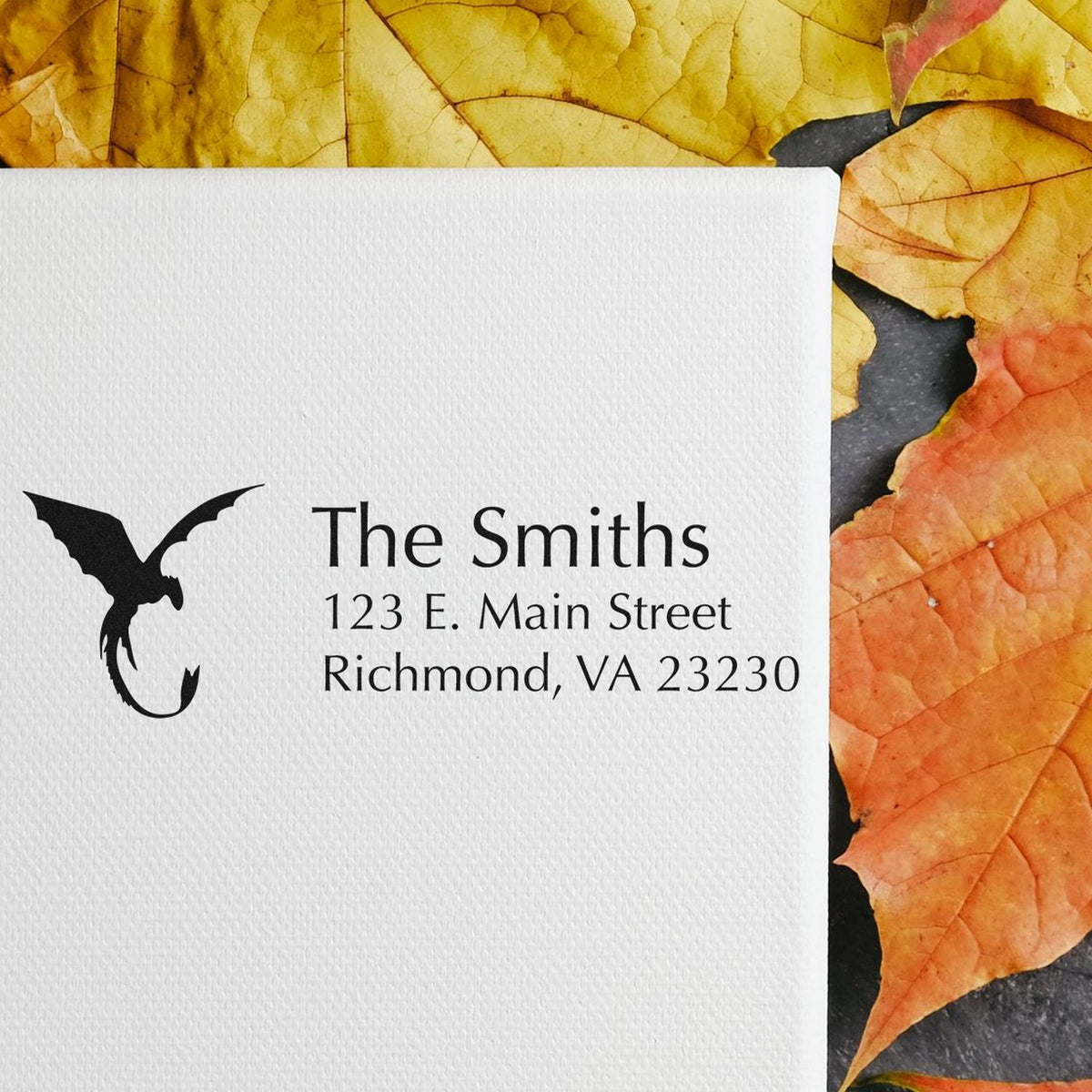 White embossed stamp card with black bird seal for The Smiths, 123 E. Main Street, on yellow and orange autumn leaves.