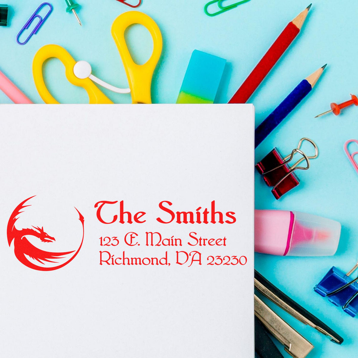 Custom red dragon stamp and seal on white paper, surrounded by colorful office supplies on a blue background.