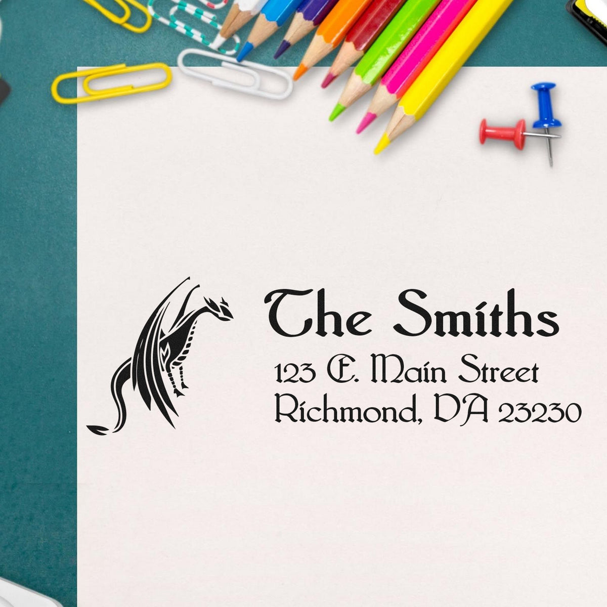 Custom black address stamp and seal for The Smiths on white paper, surrounded by colorful pencils, paper clips, and push pins.