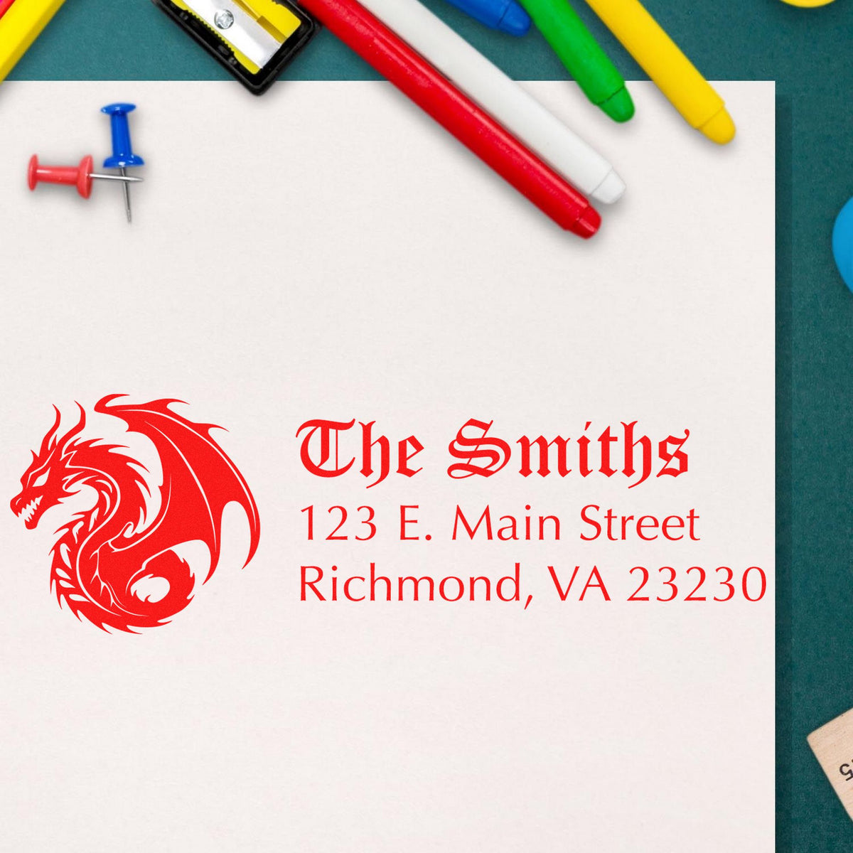 Red custom seal stamp with dragon logo and address on white paper, surrounded by colorful markers and pushpins.