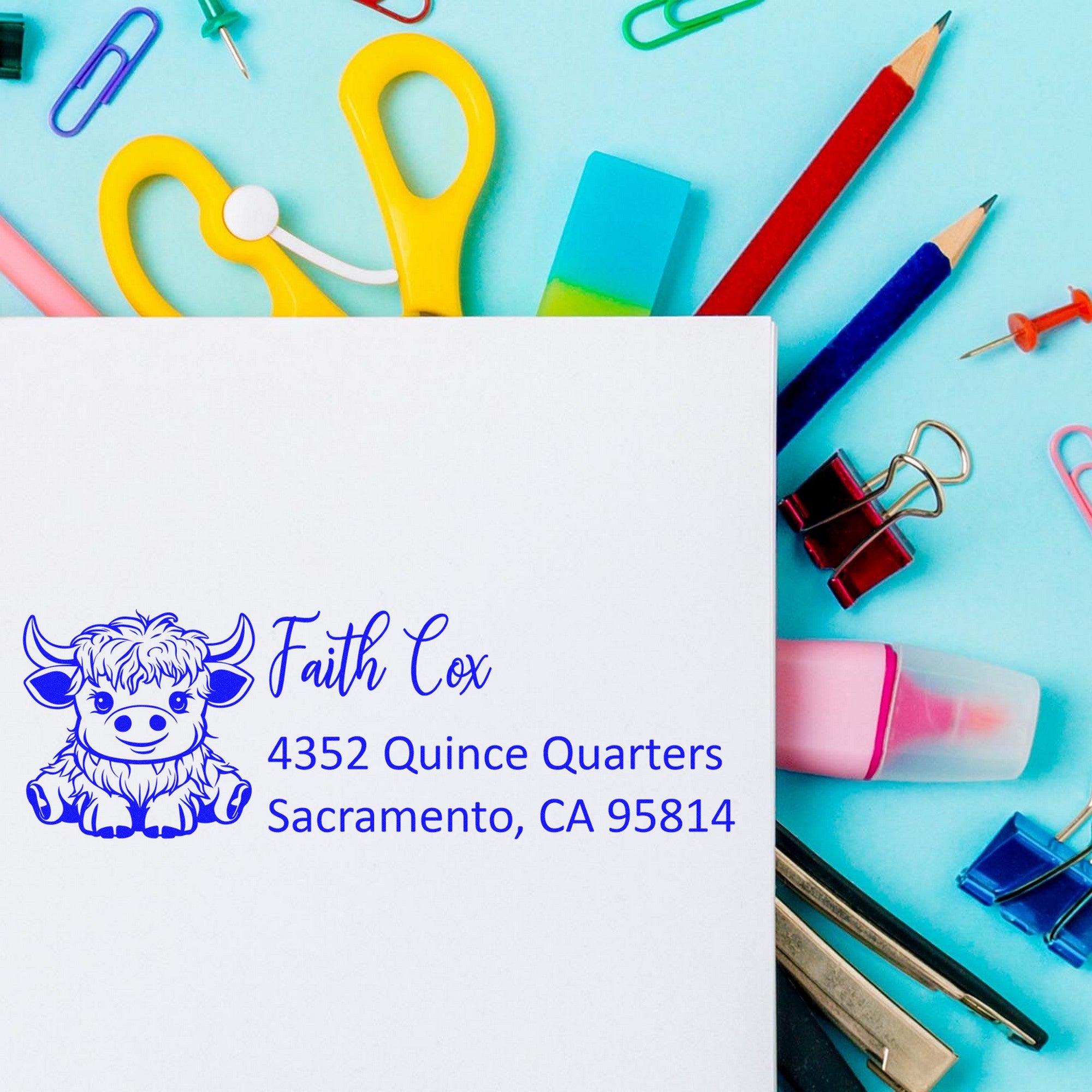 Custom blue address stamp and seal with cow logo on white paper, surrounded by colorful pencils, clips, and ink pads.