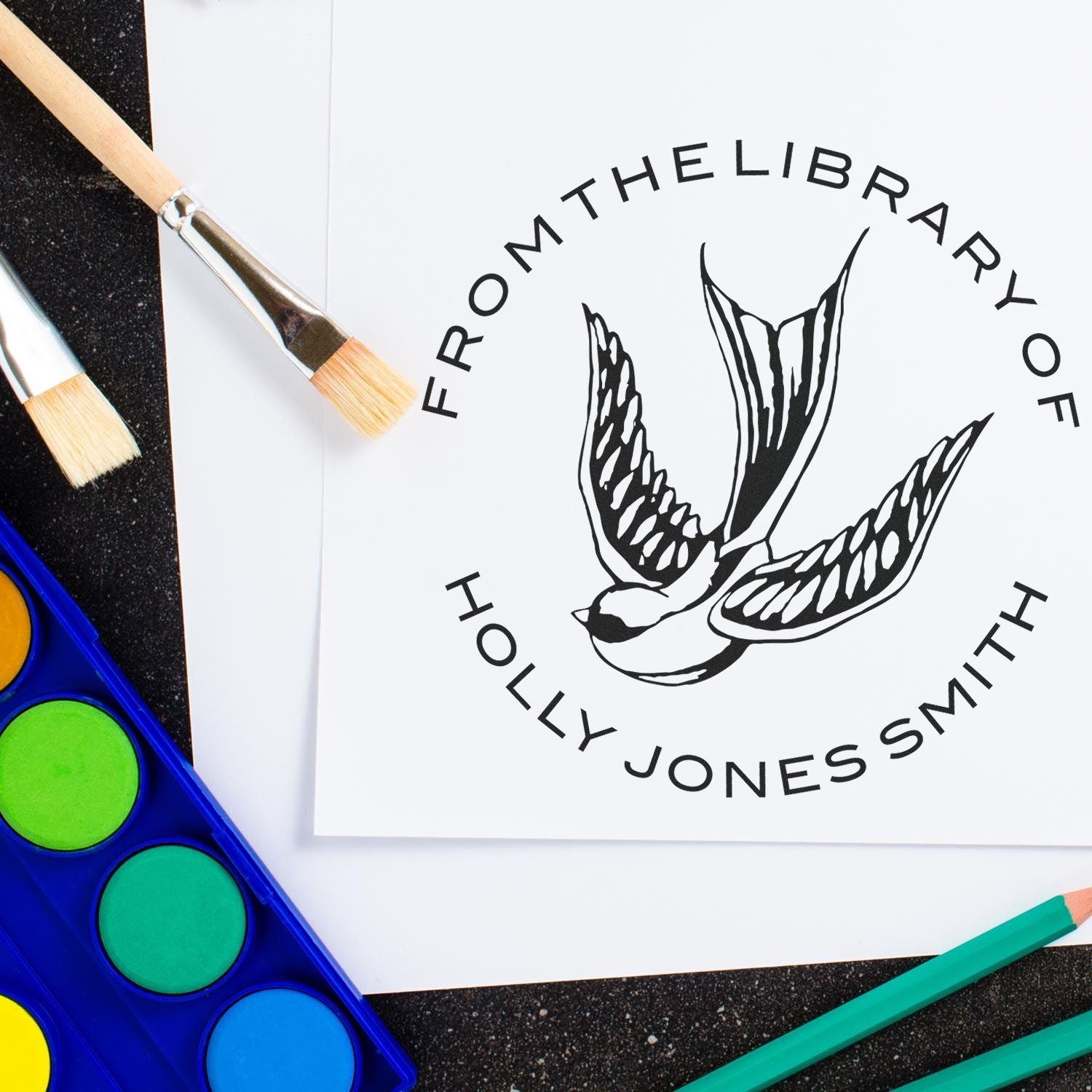 Black bird logo stamp and seal reading From the Library of Holly Jonesmith, with brushes and bright watercolor palette.