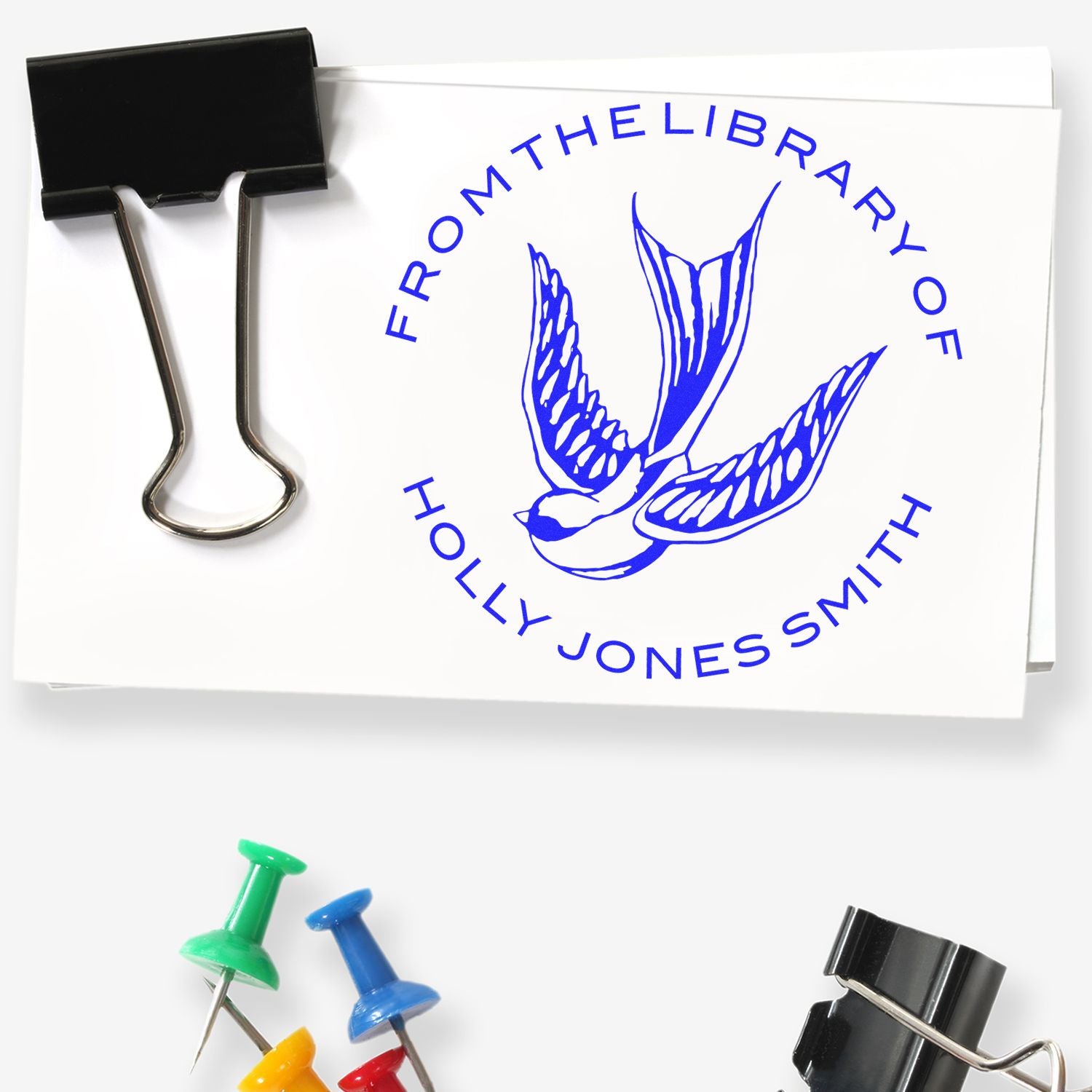 Blue custom stamp seal with bird logo and From the Library of Holly Jones Smith on white paper, clipped in black.
