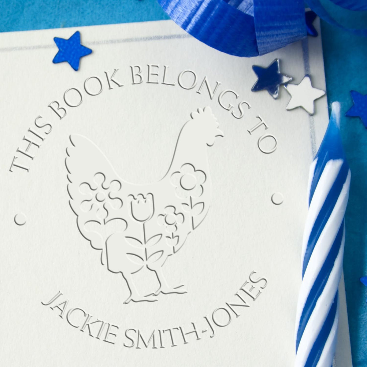 Embossed white chicken bookplate seal with blue stars and ribbon, reading This Book Belongs To Jackie Smith-Jones.