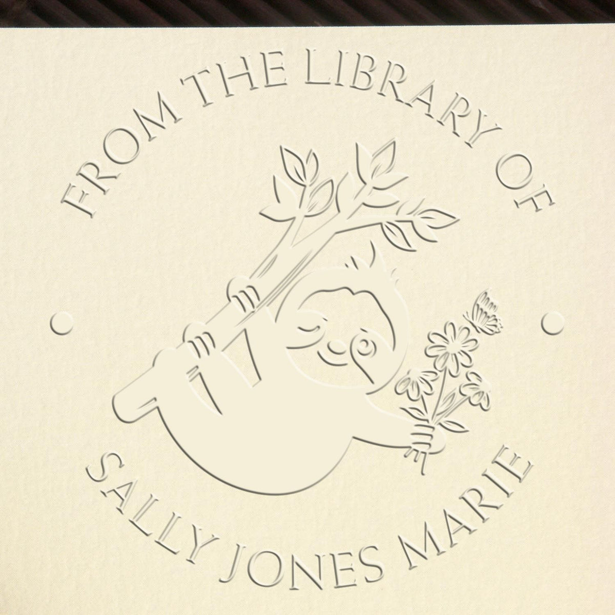 Cream embossed custom library seal stamp with sloth, branch, and flowers; reads From the Library of Sally Jones Marie.