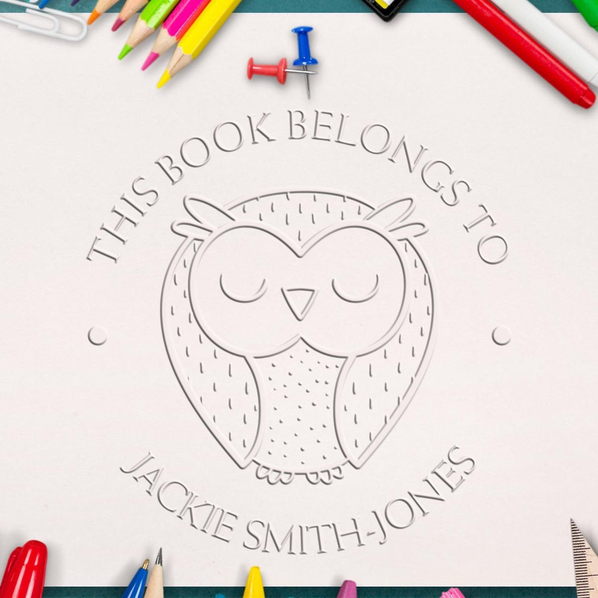Custom owl bookplate stamp and seal on white paper, surrounded by colorful pencils and red-blue pushpins.