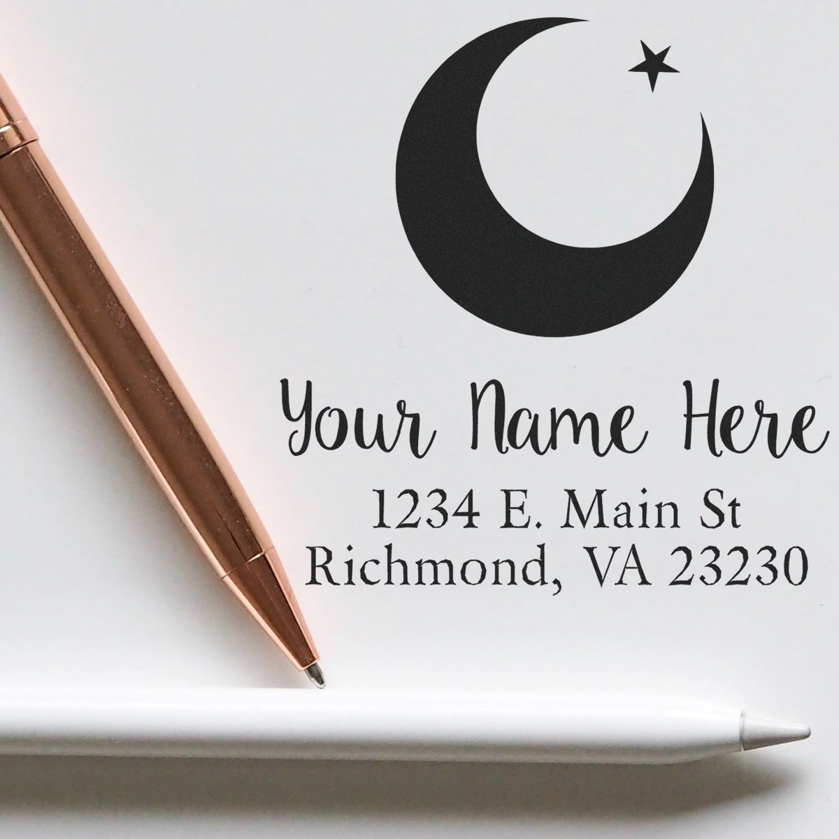 Custom black crescent moon and star stamp seal with name and address, beside a rose-gold pen and white stylus.