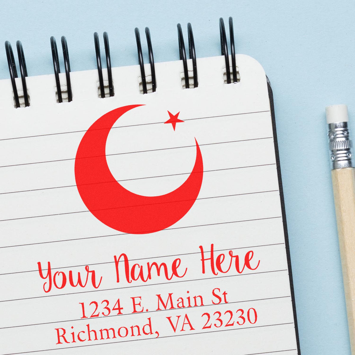 Red crescent-and-star custom stamp seal on a white spiral notepad with red address text, beside a pencil on a light blue background.