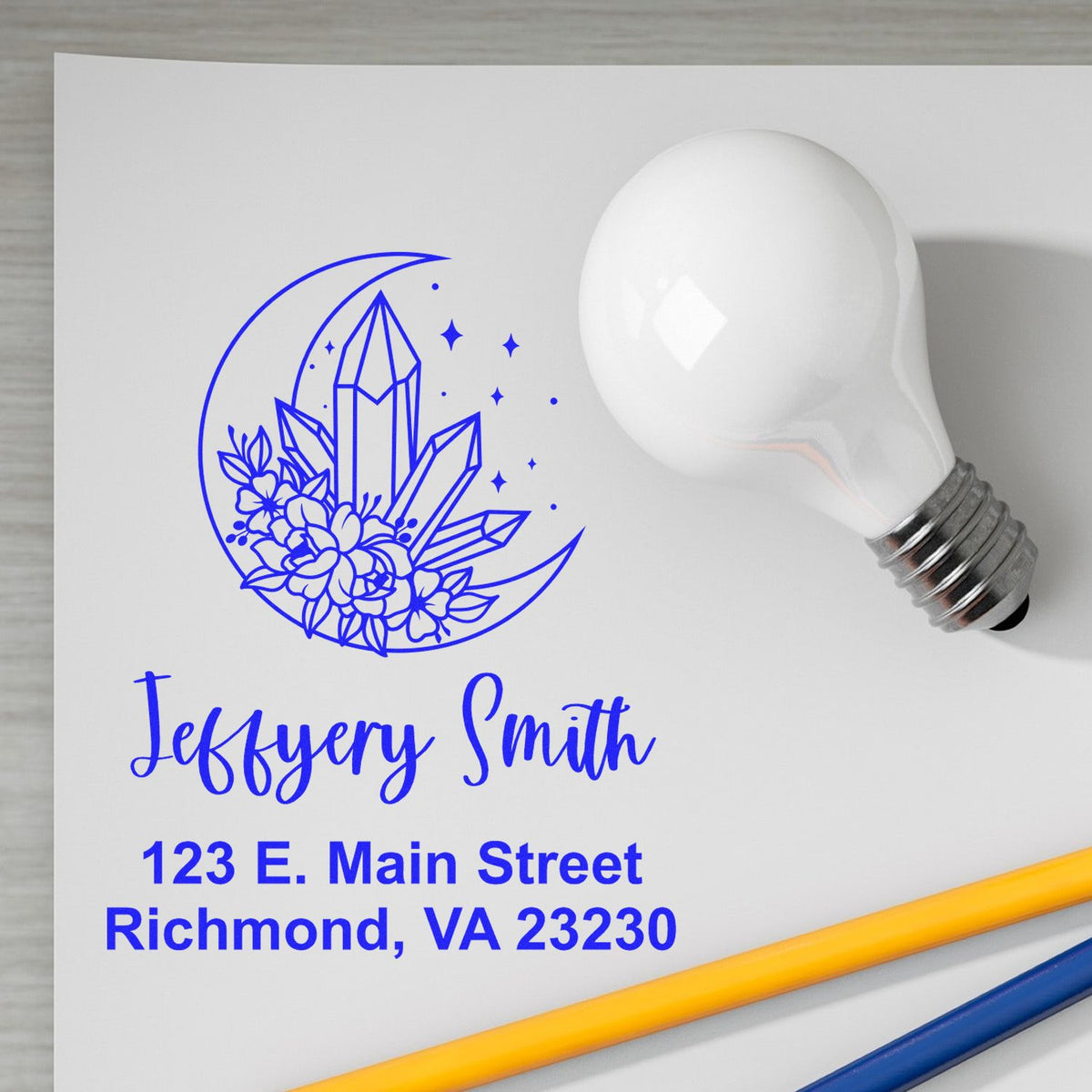 Blue custom stamp and seal proof with crystal moon logo, name, and address beside a white light bulb.