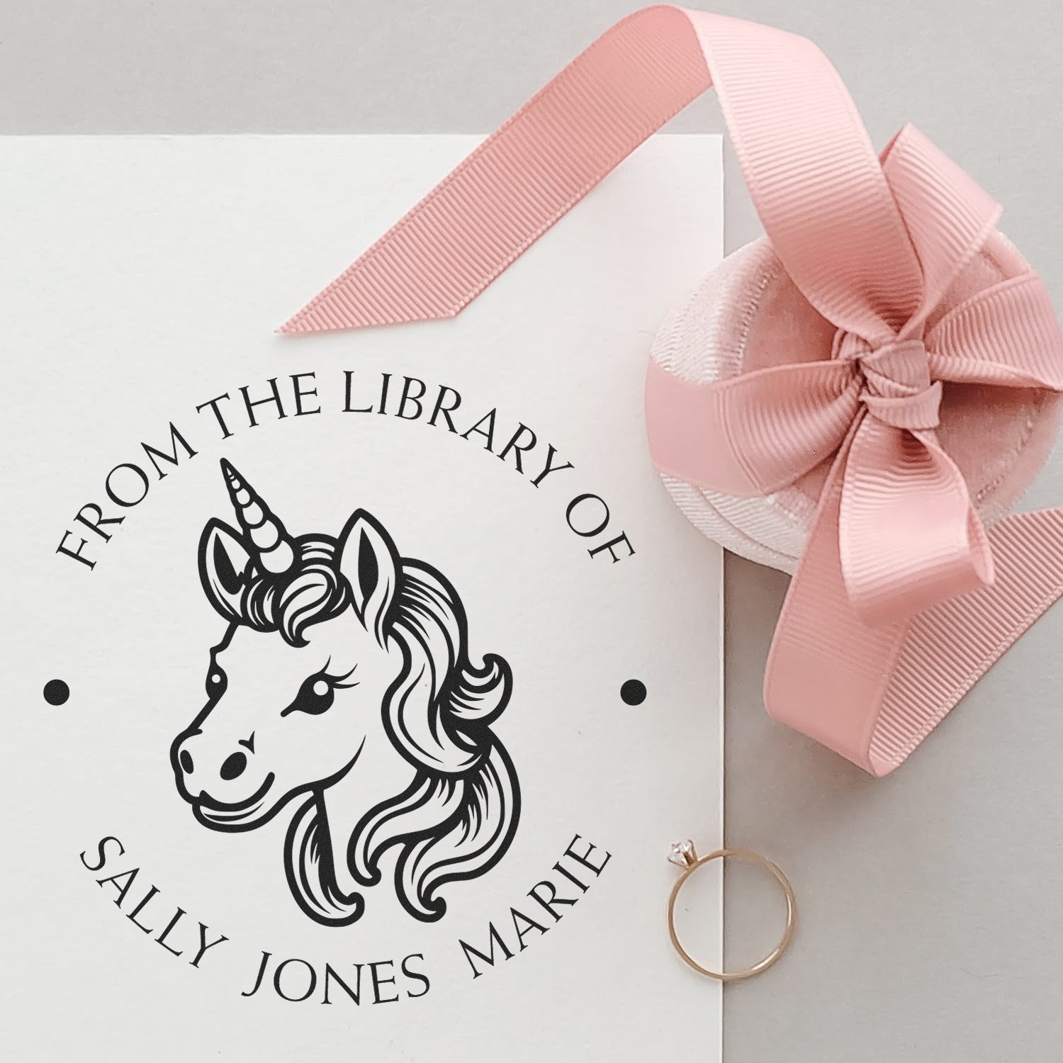Black unicorn library stamp on white card with pink ribbon seal and gold ring, personalized for Sally Jones Marie.