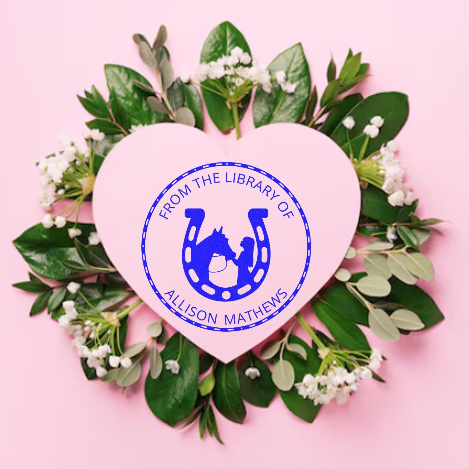 Pink heart-shaped custom stamp seal with blue horseshoe horse logo, surrounded by green leaves and white flowers.