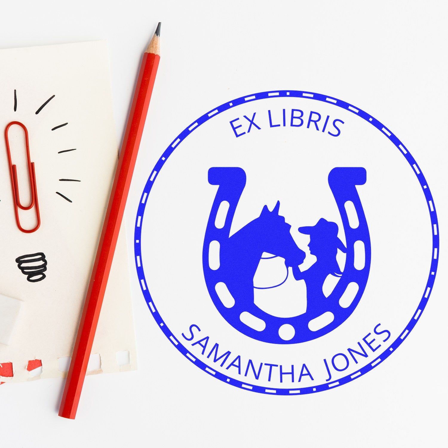 Blue ex libris horse-and-rider stamp seal with Samantha Jones, beside a red pencil and paperclip.