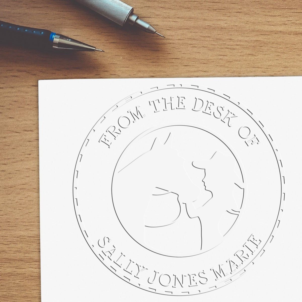 Custom white embossed desk seal on paper, with horse profile branding and pens on a wood desk.