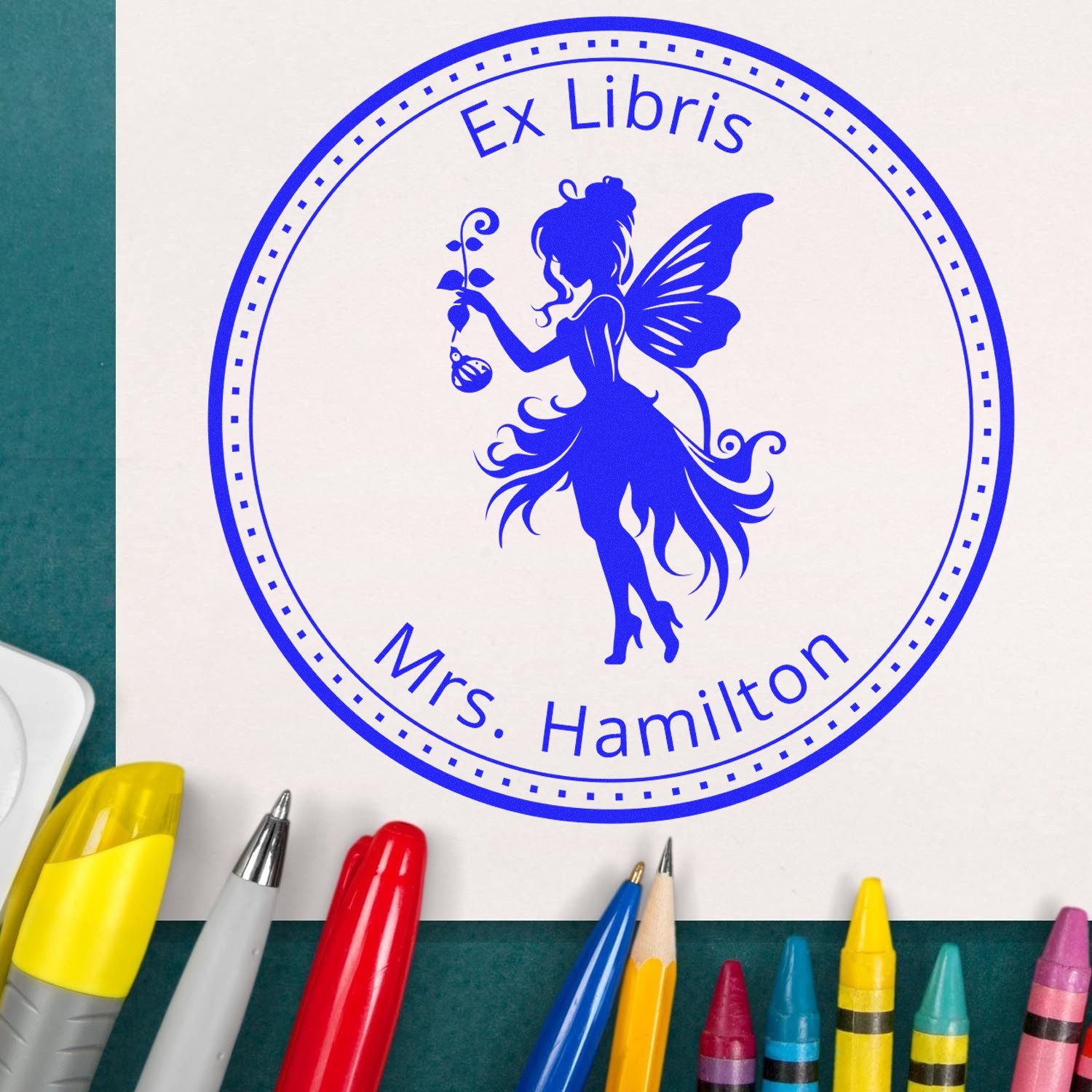 Blue Ex Libris stamp seal with fairy silhouette and Mrs. Hamilton text, surrounded by colorful pens.