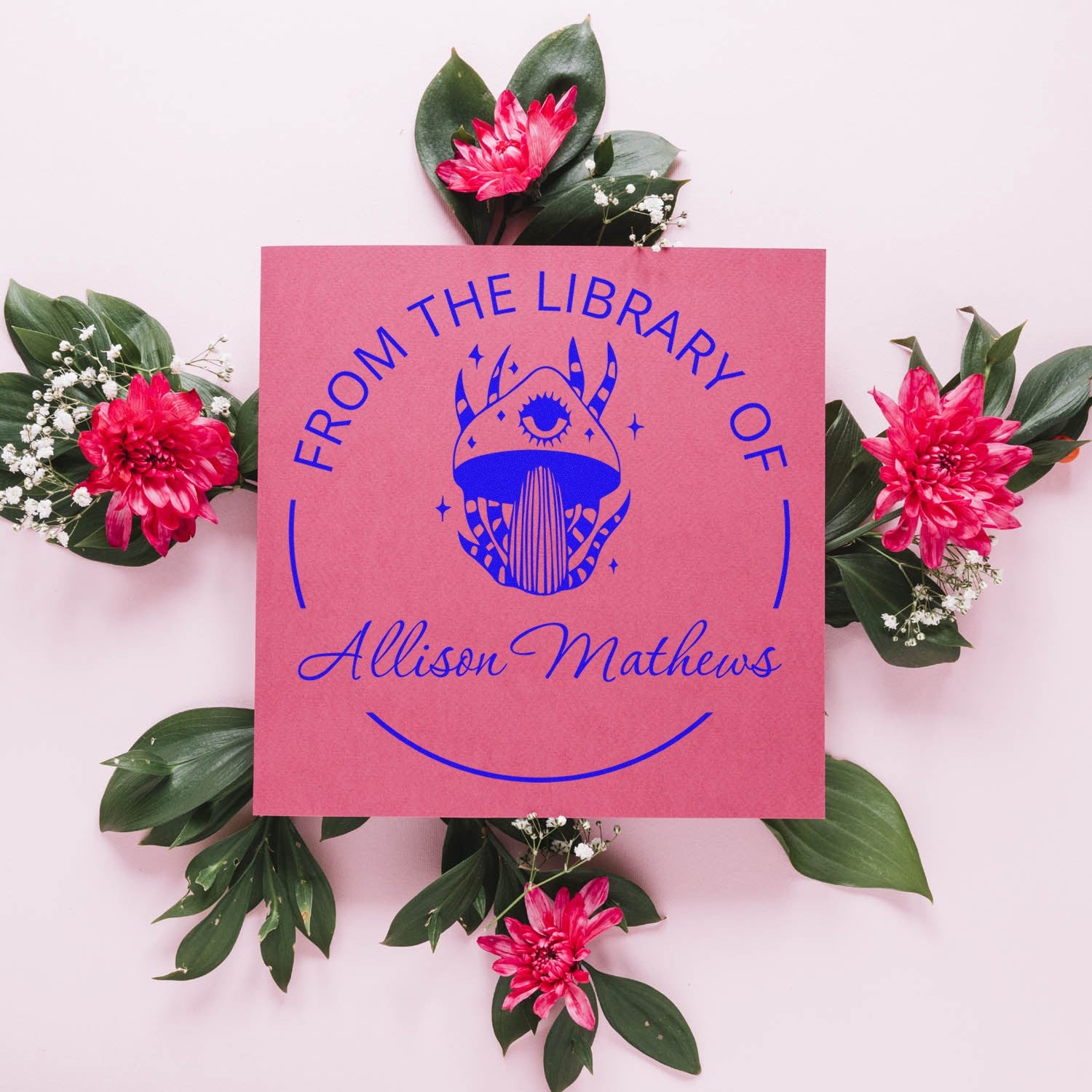 Pink custom library stamp and seal with blue owl emblem and From the Library of Allison Mathews text, framed by green leaves and pink flowers.