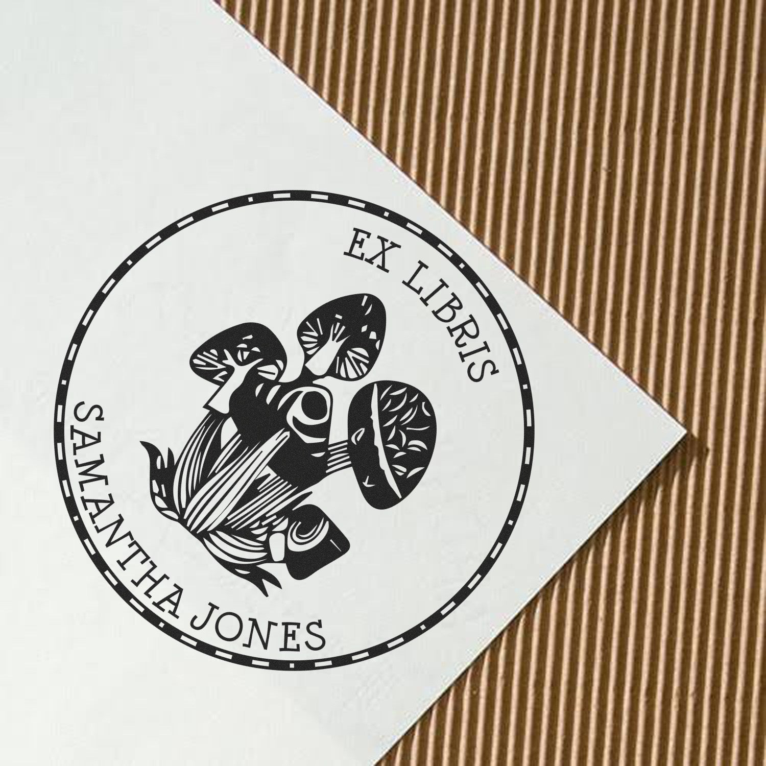 Black custom ex libris stamp seal with mushroom illustration on white paper over brown corrugated background.